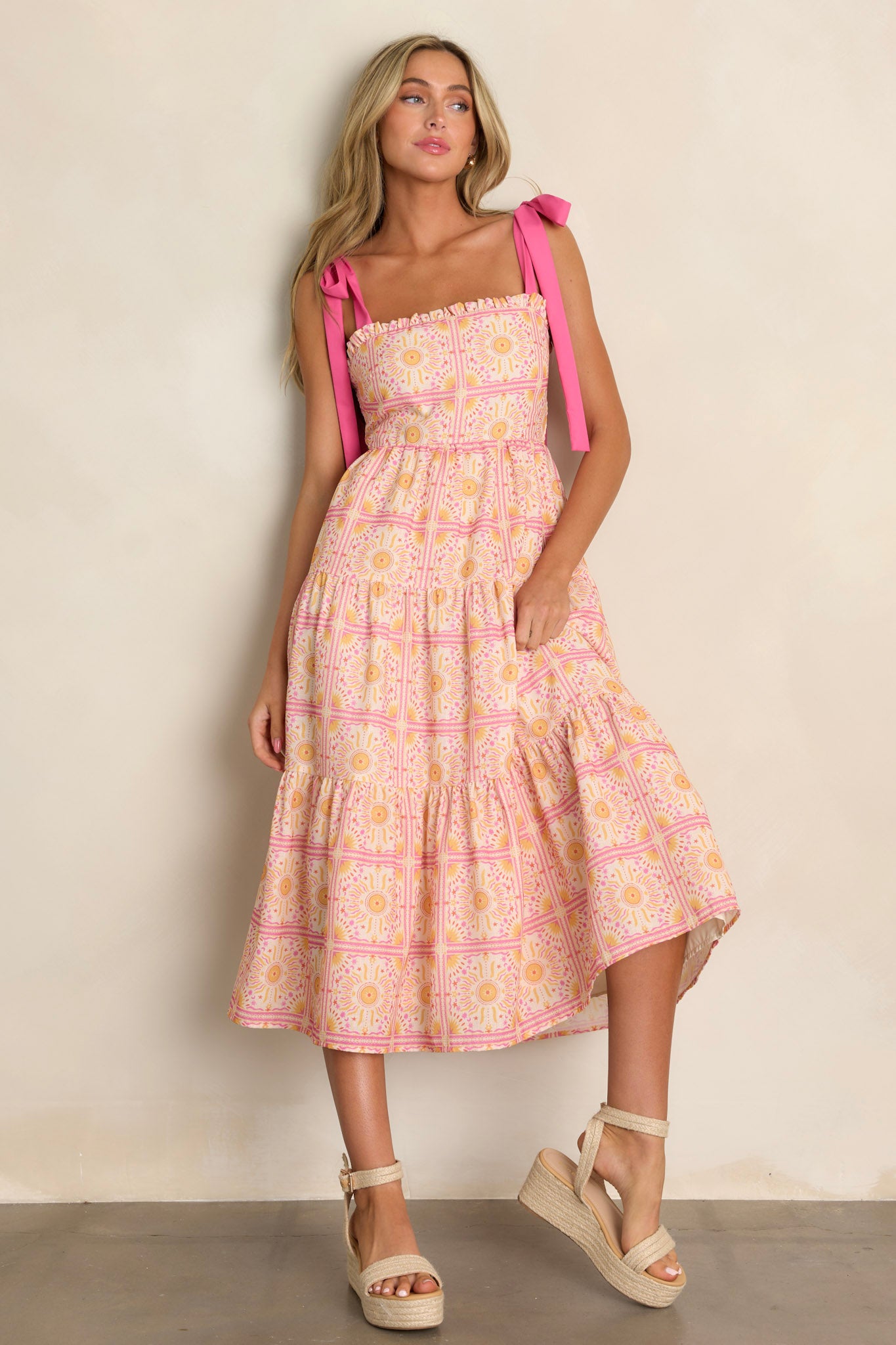 Full length view of a pink multi midi dress with a ruffled square neckline, a fully smocked back, a tiered design, a unique print, and a flowing silhouette
