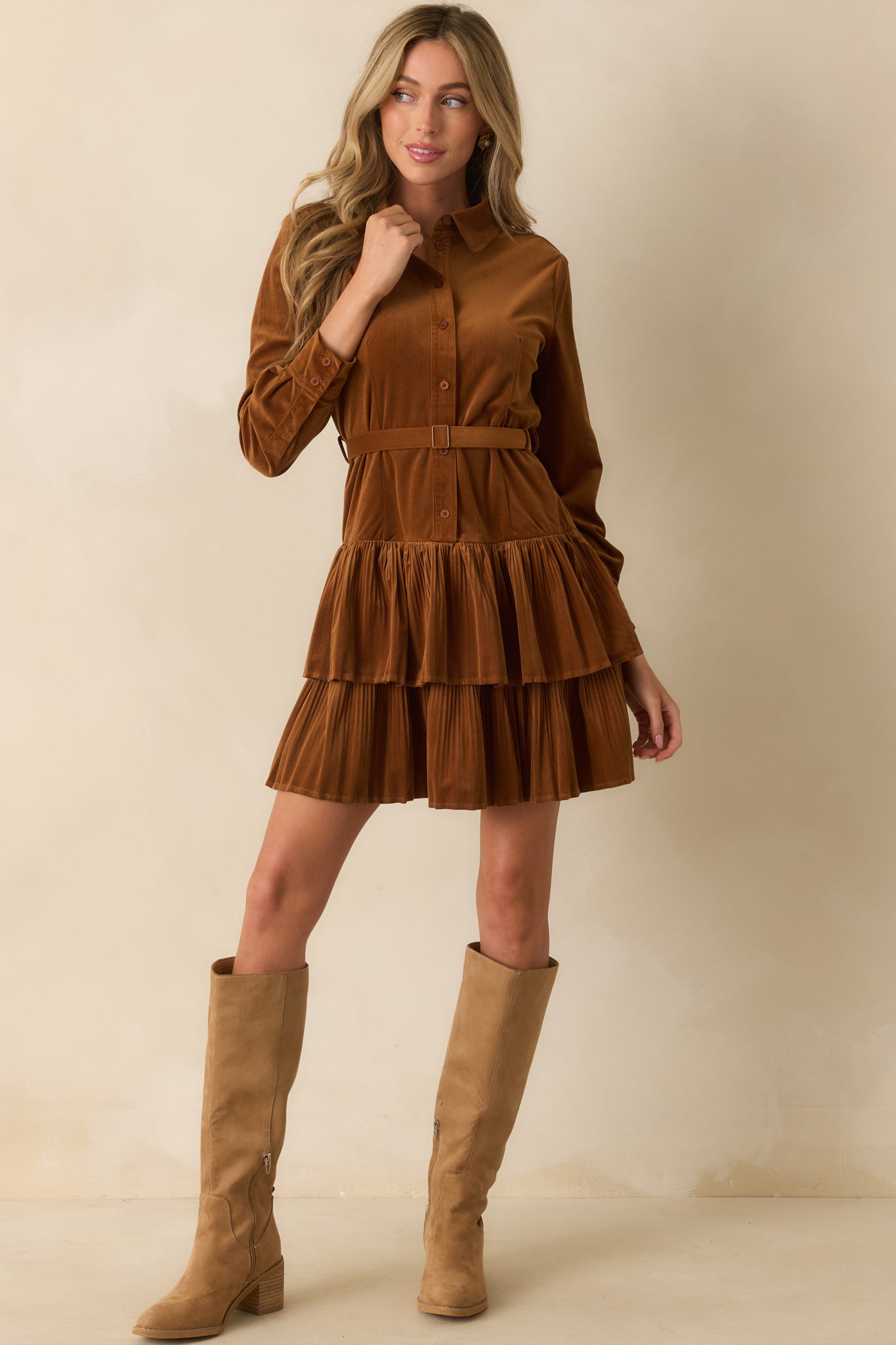 Caramel brown corduroy mini dress with collared neckline, long sleeves with button cuffs, optional self-tie belt, and tiered skirt.