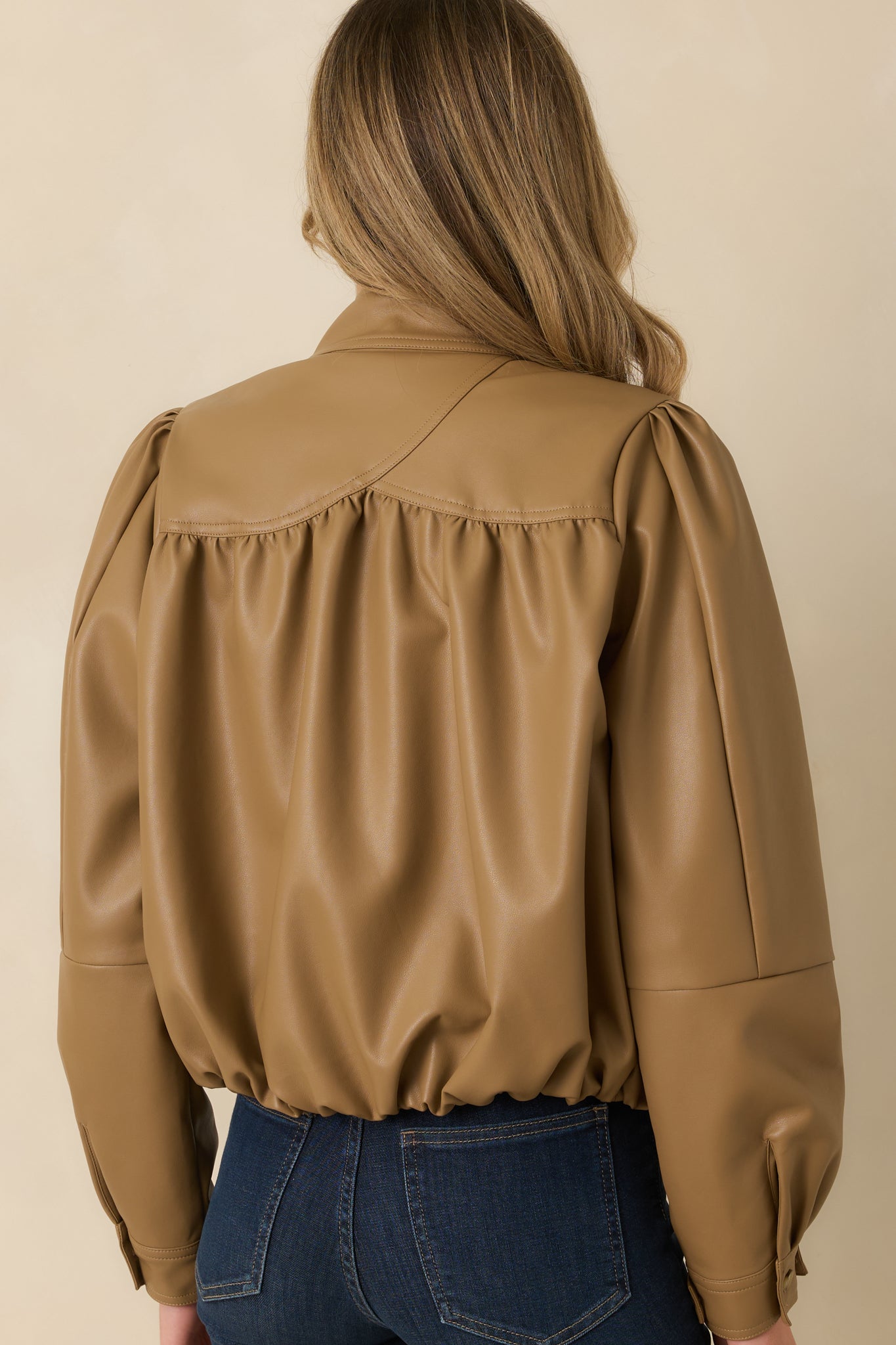 Rear view of the caramel vegan leather jacket featuring gathered back yoke detailing, long puff sleeves, and an elasticized hem.