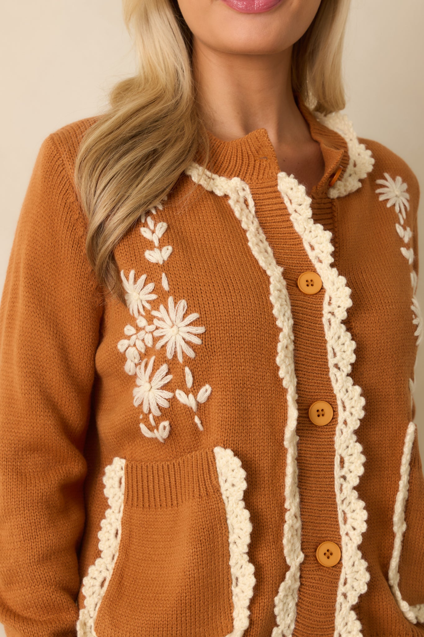 A close-up of the cardigan fabric showing ivory daisy embroidery, crochet trim, and knit texture.