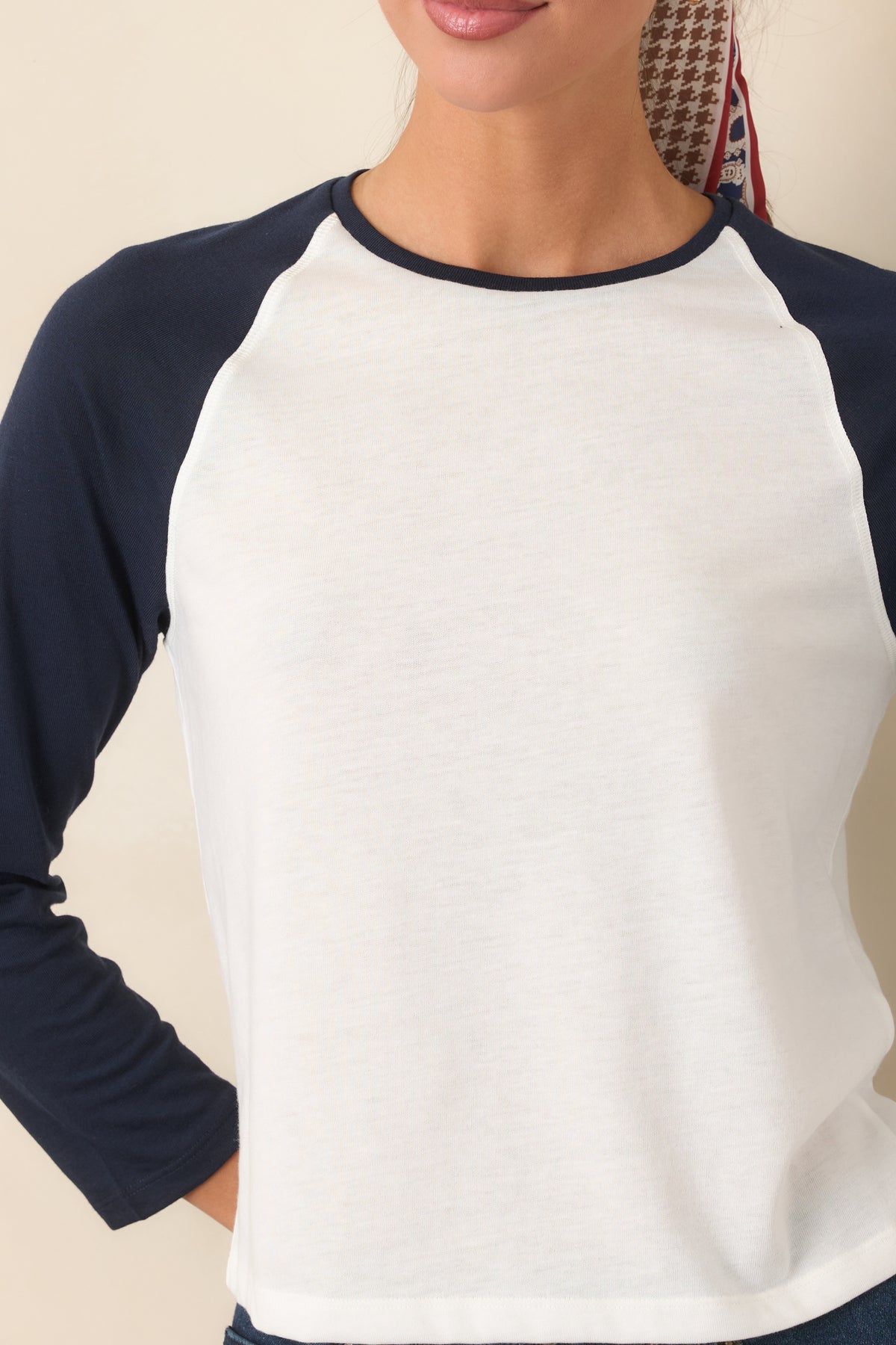Close-up of the chalk white fabric, navy raglan sleeve, and contrasting crew neckline trim.