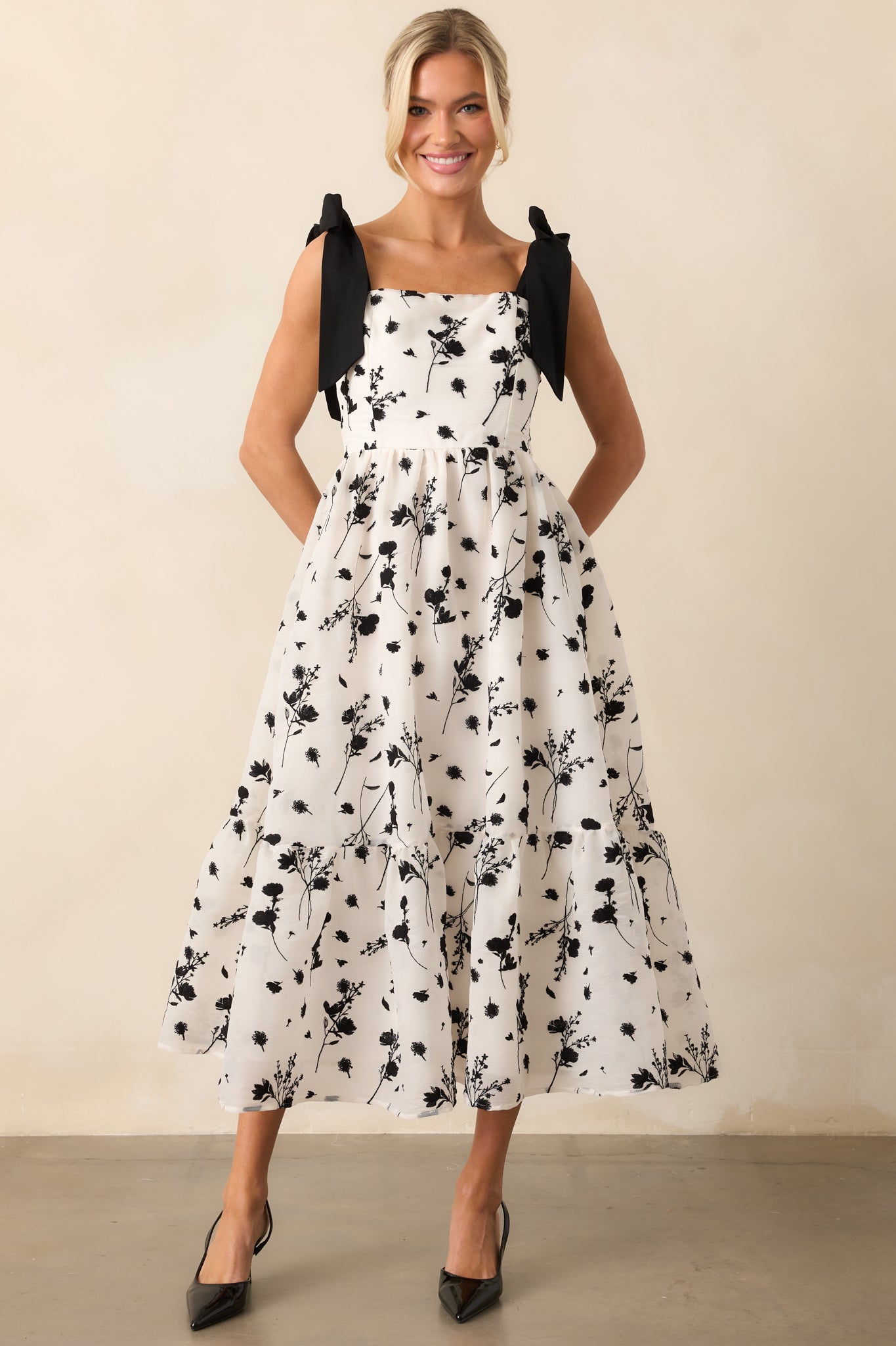 A chic midi dress with black floral embroidery and a square neckline, enhanced by a smocked back and self-tie bow straps for a tailored feel.