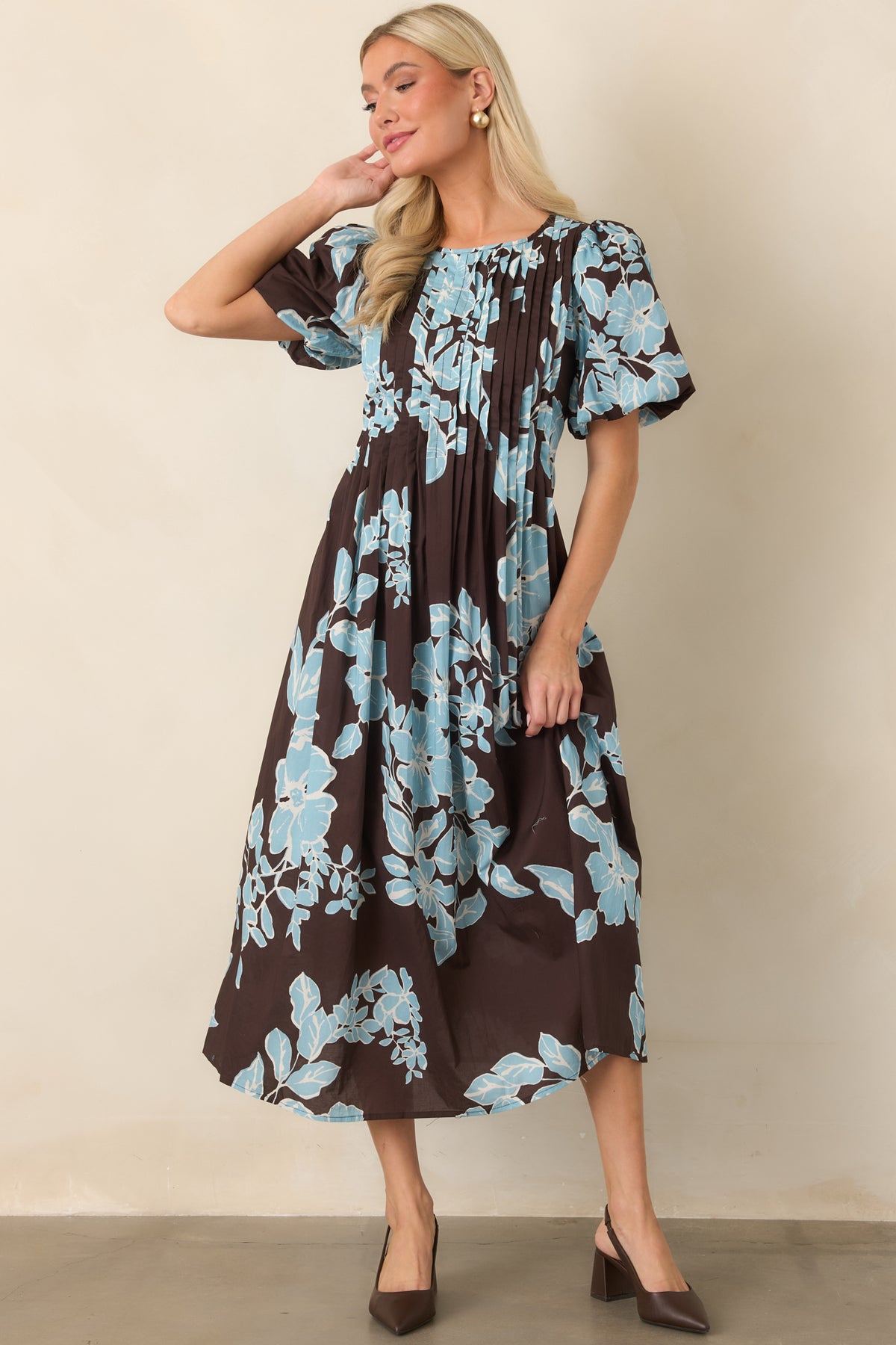 Chocolate midi dress featuring oversized light blue blooms, short puff sleeves, a defined waist, and gently flared skirt.