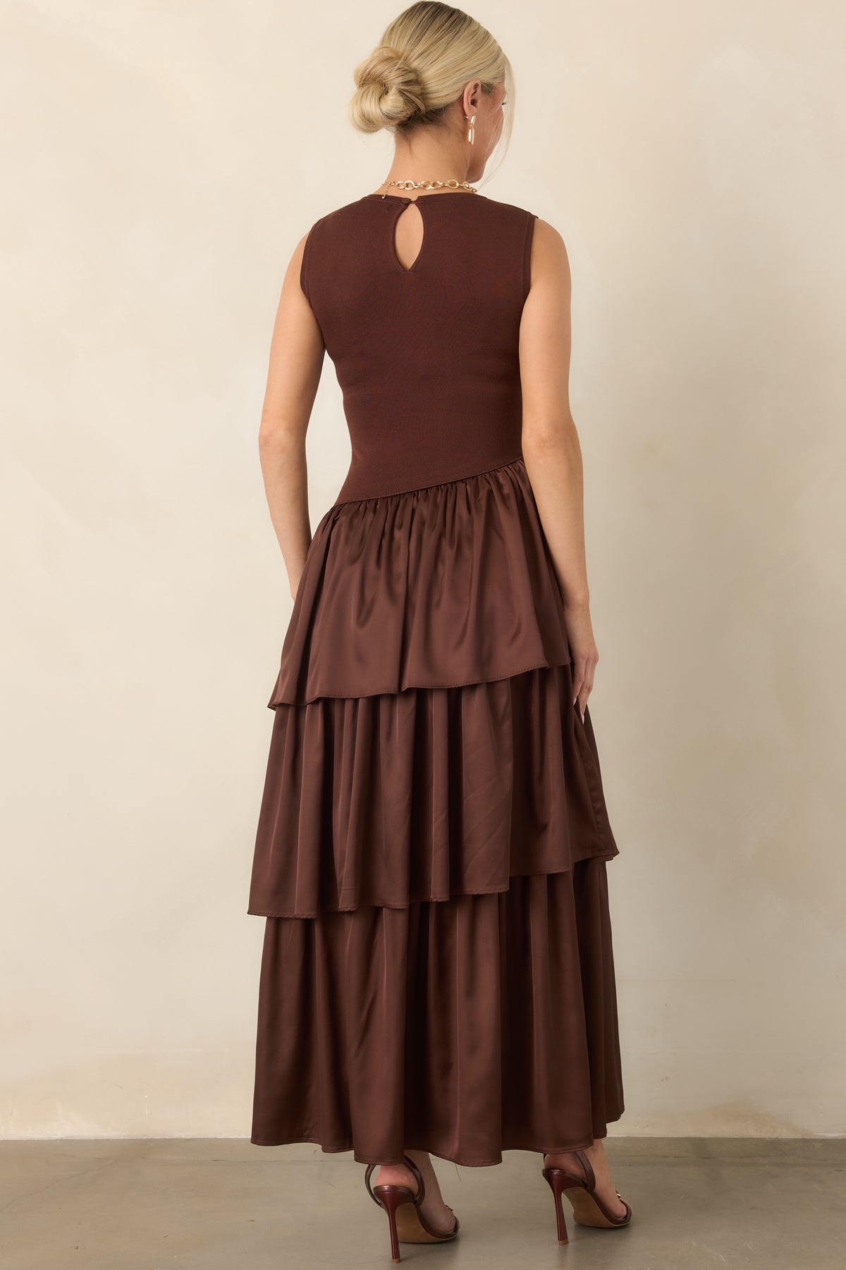 Rear view shows the chocolate brown dress with a buttoned keyhole closure at the back neckline and layered skirt.