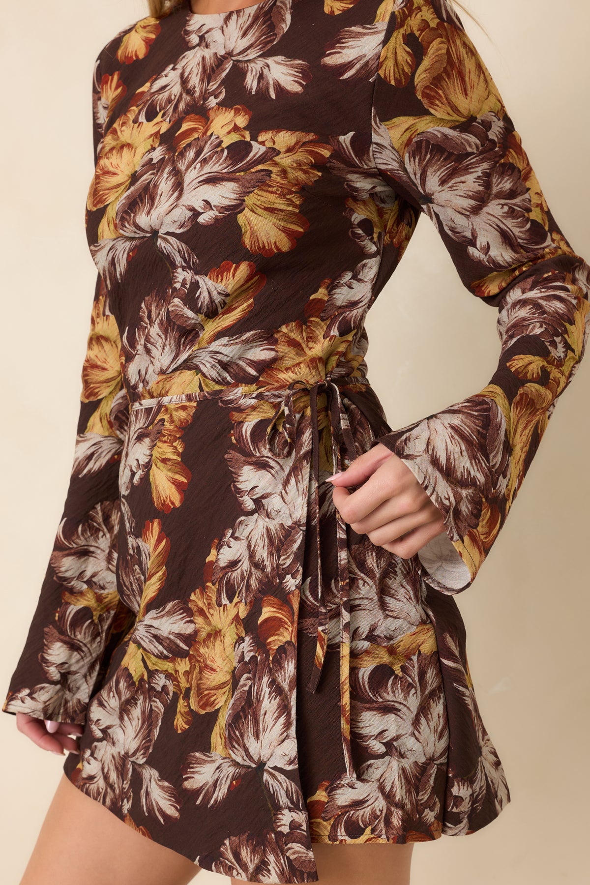 Side tie and overlapping wrap panels create gathered draping across the waist of the chocolate brown floral dress.