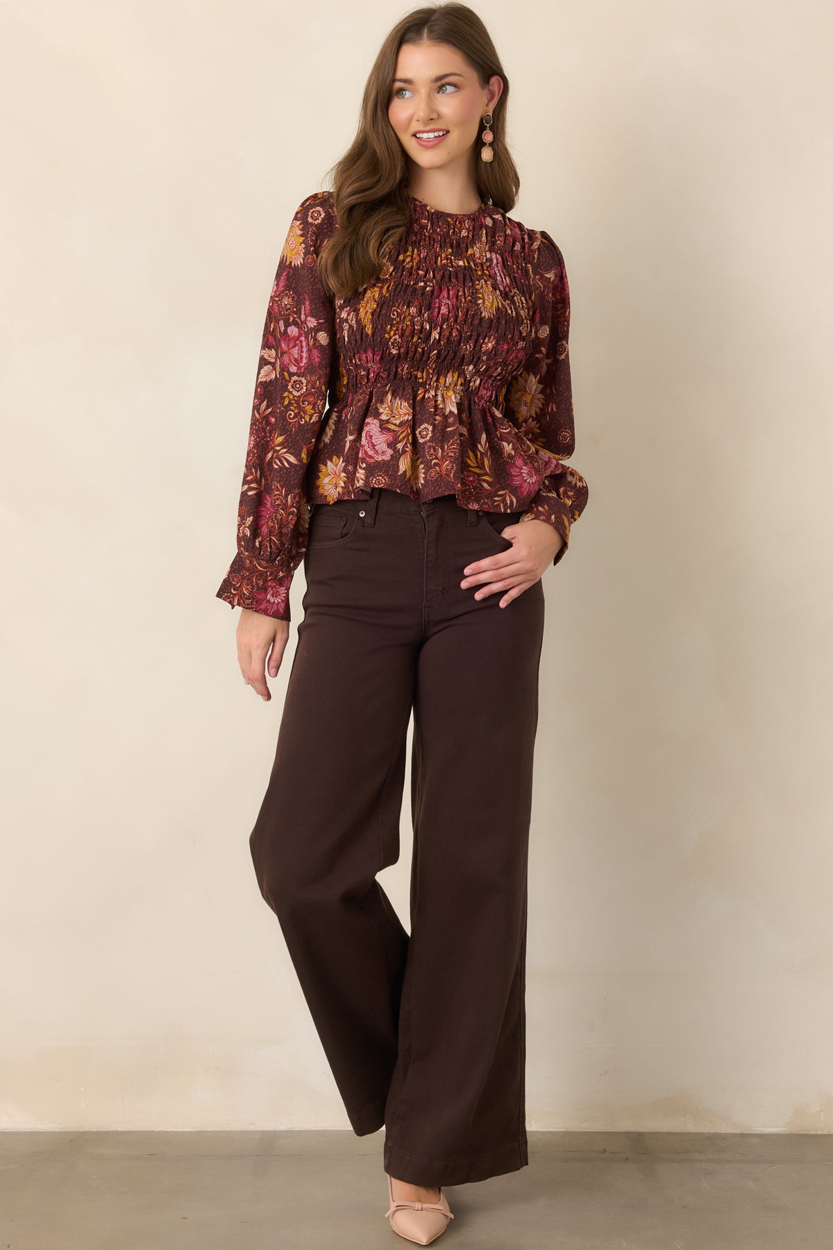 Chocolate brown top with a pink, ivory, rust, and golden yellow floral print, smocked bodice, round neckline, long puff sleeves, and flared peplum hem.