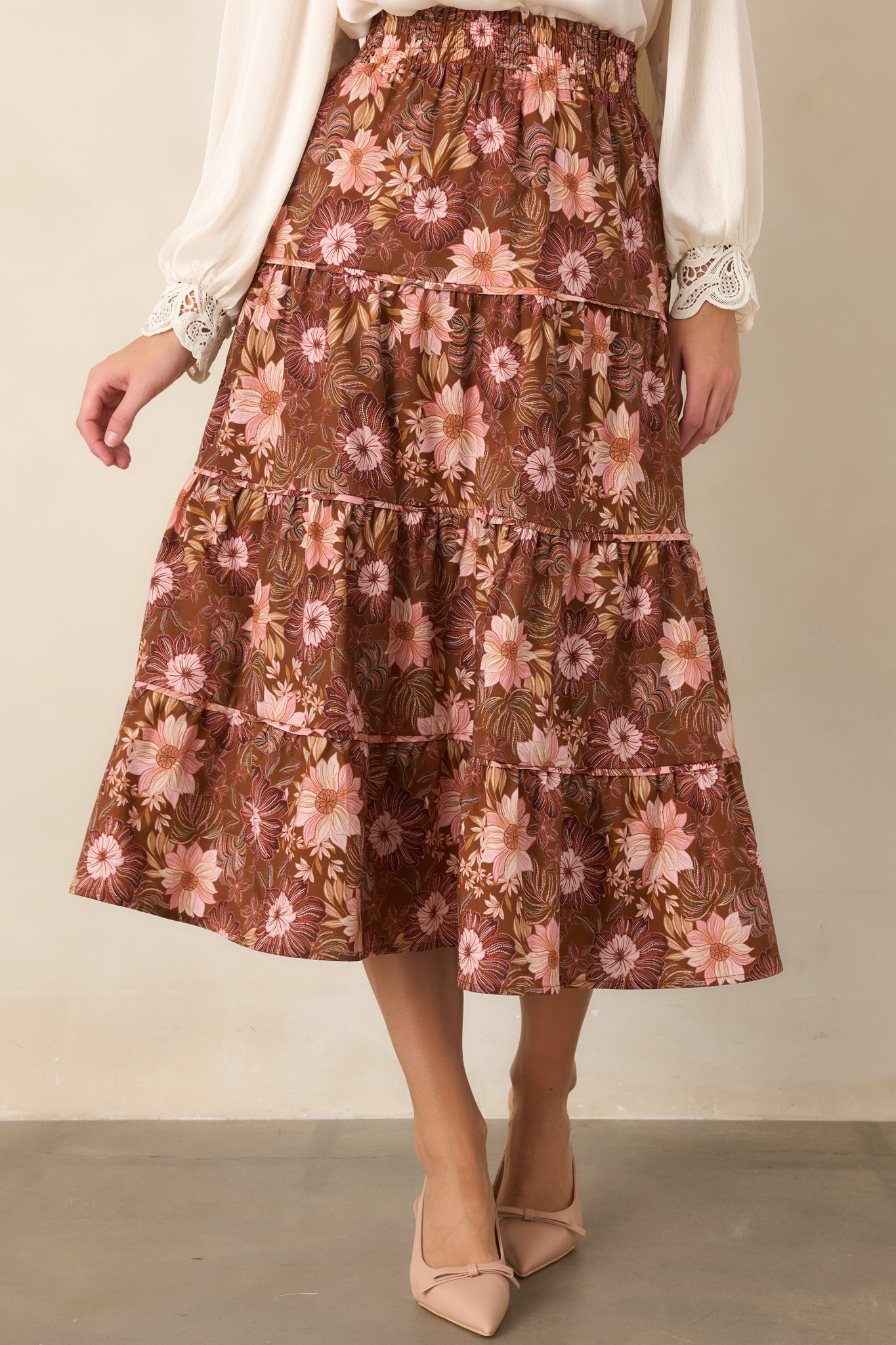 Floral midi skirt in warm chocolate brown with layered tiers, a softly gathered shape, and colorful pink, burgundy, and muted green blooms.