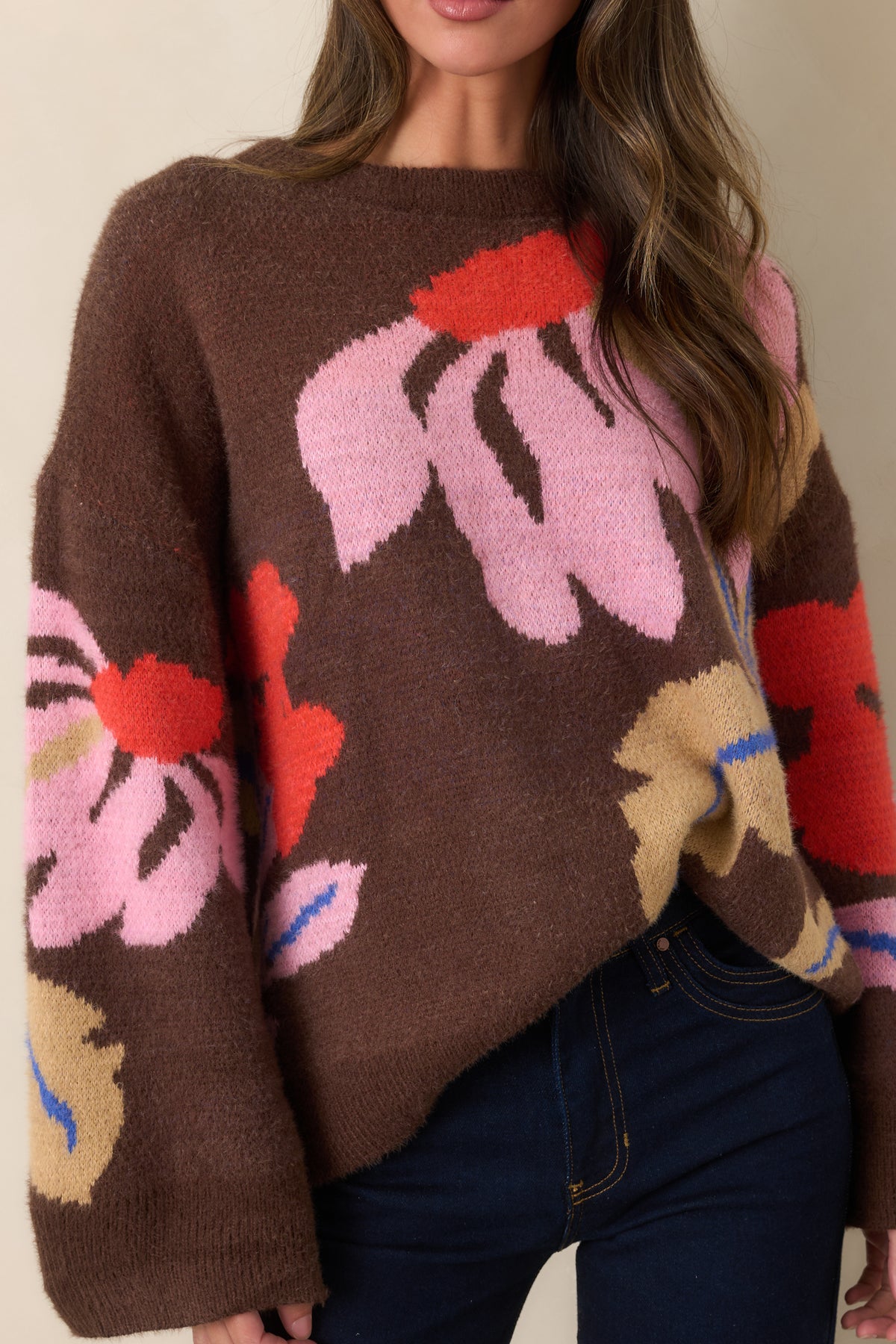 Close-up of oversized floral intarsia motifs in pink, red-orange, camel, and cobalt against chocolate-brown knit.