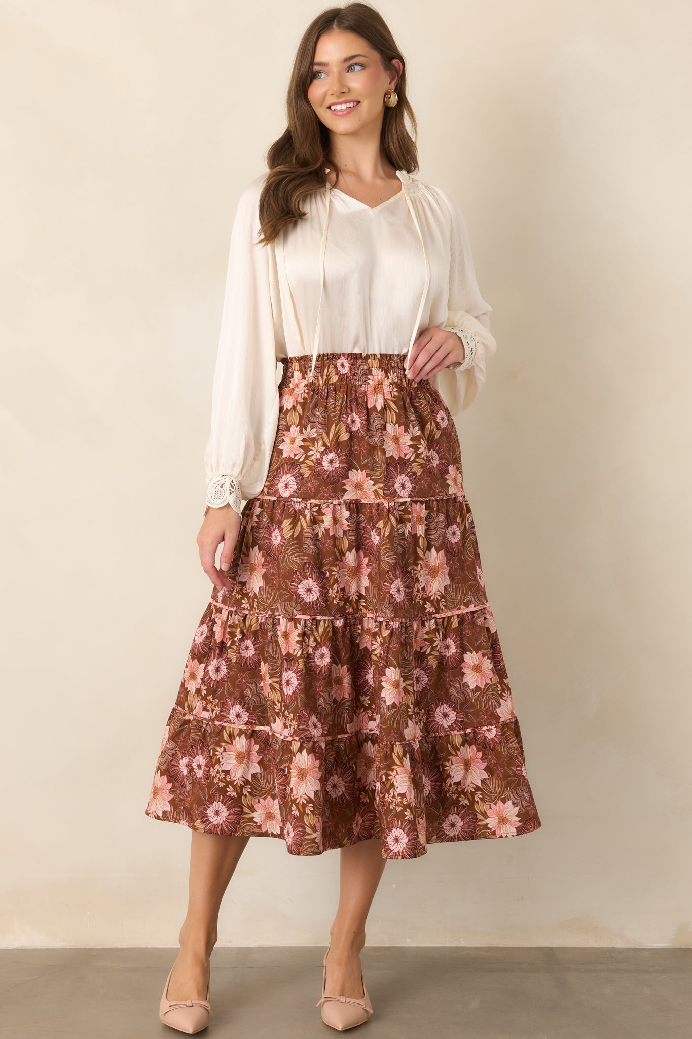 Chocolate brown midi skirt covered in soft pink, burgundy, and muted green florals, featuring a smocked elastic waistband and tiered flowing silhouette.