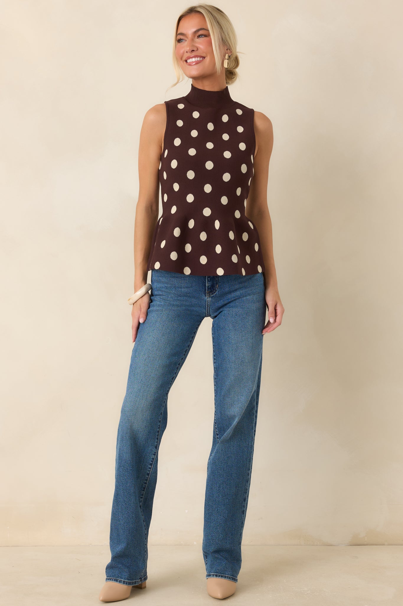 Chocolate brown sleeveless sweater top featuring a mock neckline, fitted shape, and feminine peplum finish.