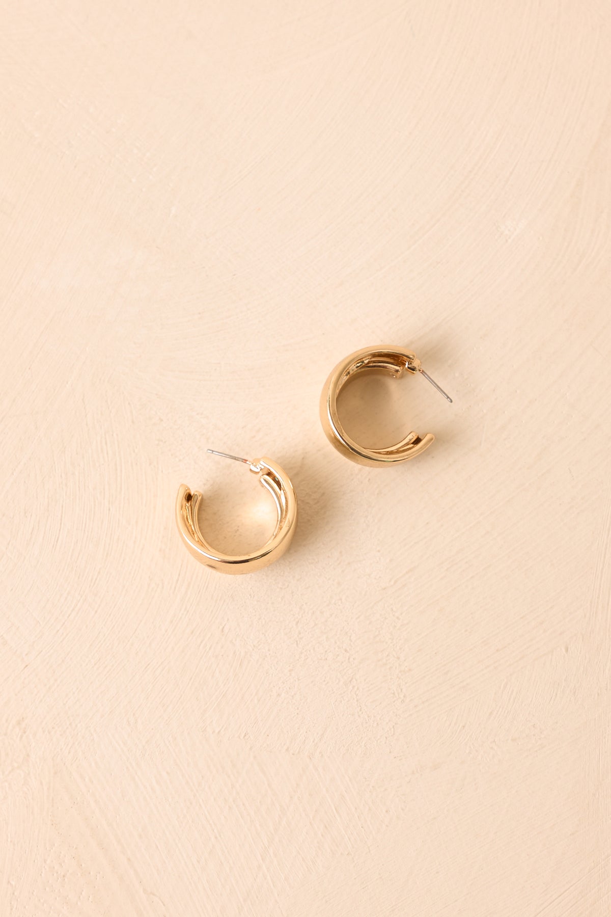 Chunky gold-tone earrings highlighting the rounded silhouette, sculptural construction, and reflective polished finish.