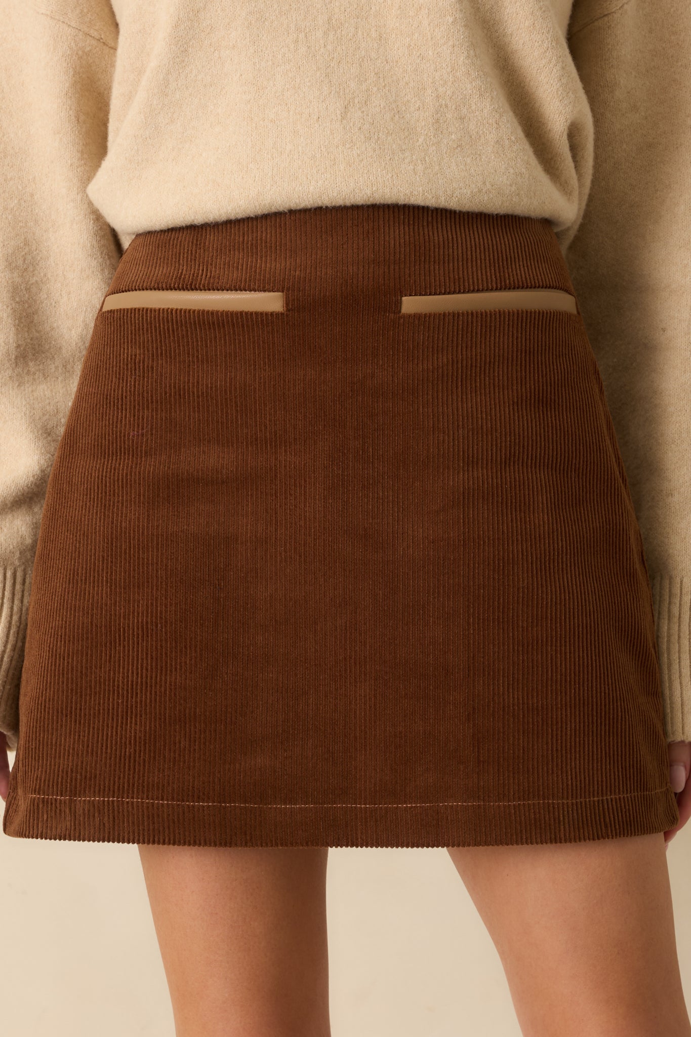 Cinnamon brown mini skirt with high-waisted fit, faux front pockets with contrast trim, and smooth cotton corduroy fabric.