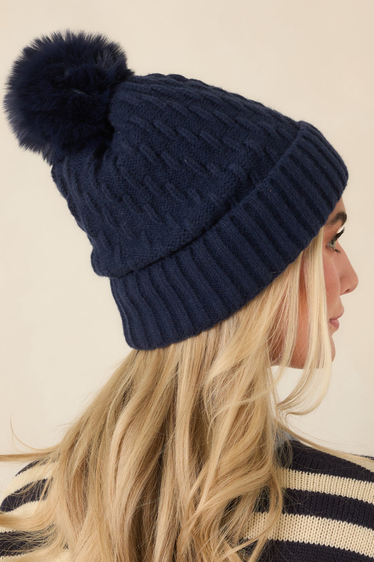 Classic cable stitching runs across the knit hat, finished with a fluffy tonal pom and a folded ribbed brim.