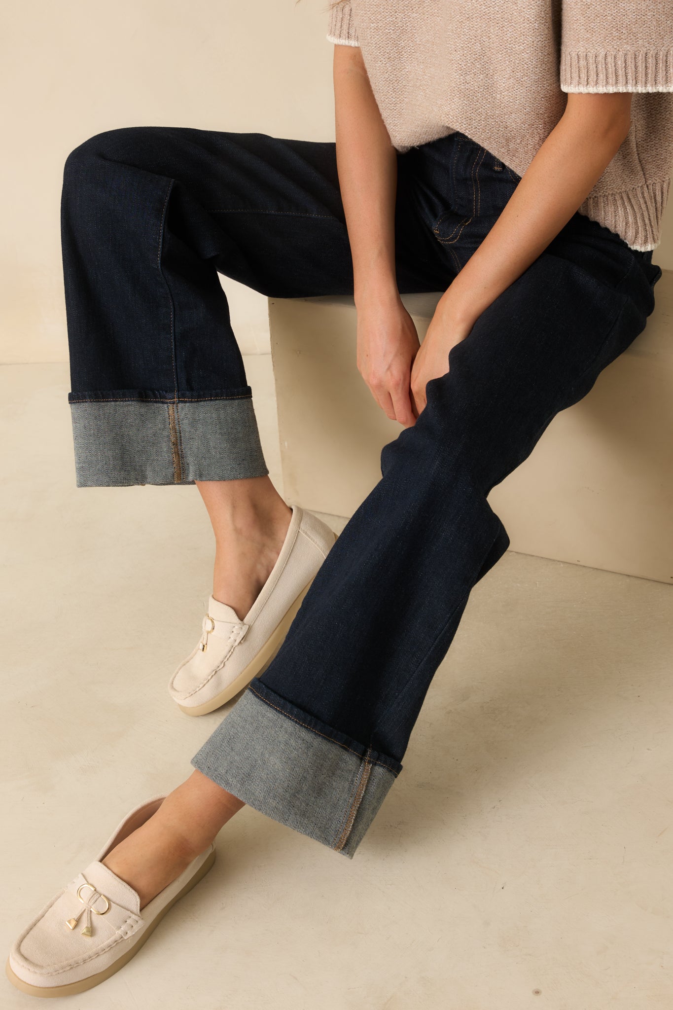 Close crop showing high-rise waistband, button closure, and front pocket detail on dark wash jeans.