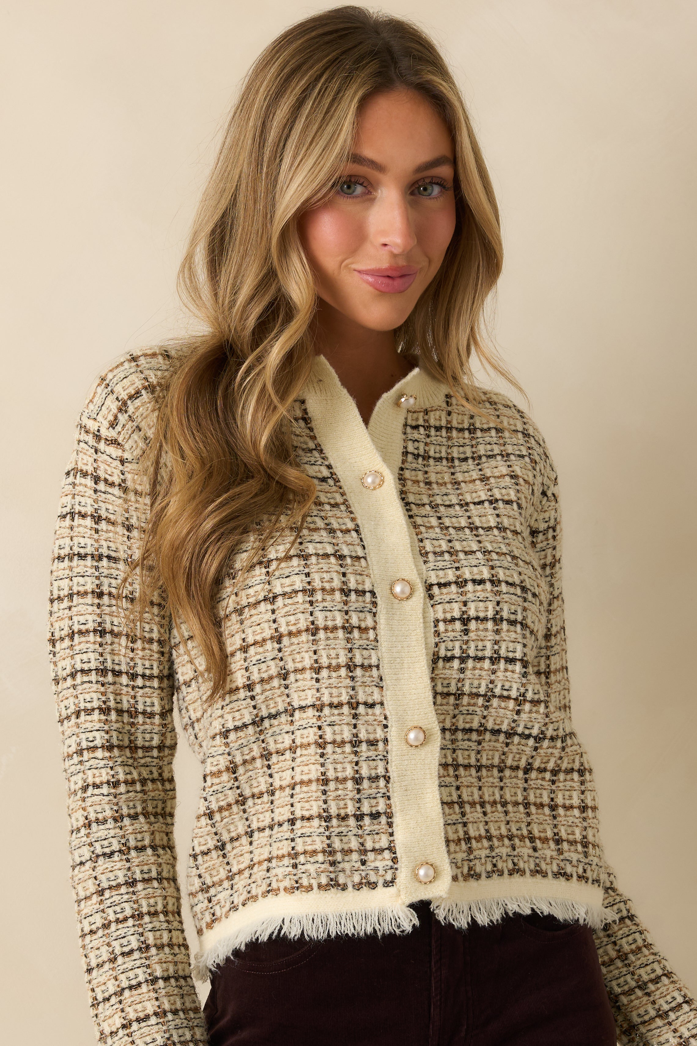 Close crop showing cardigan’s front patch pockets, pearl buttons, and plaid pattern in ivory, black, caramel, and gold.