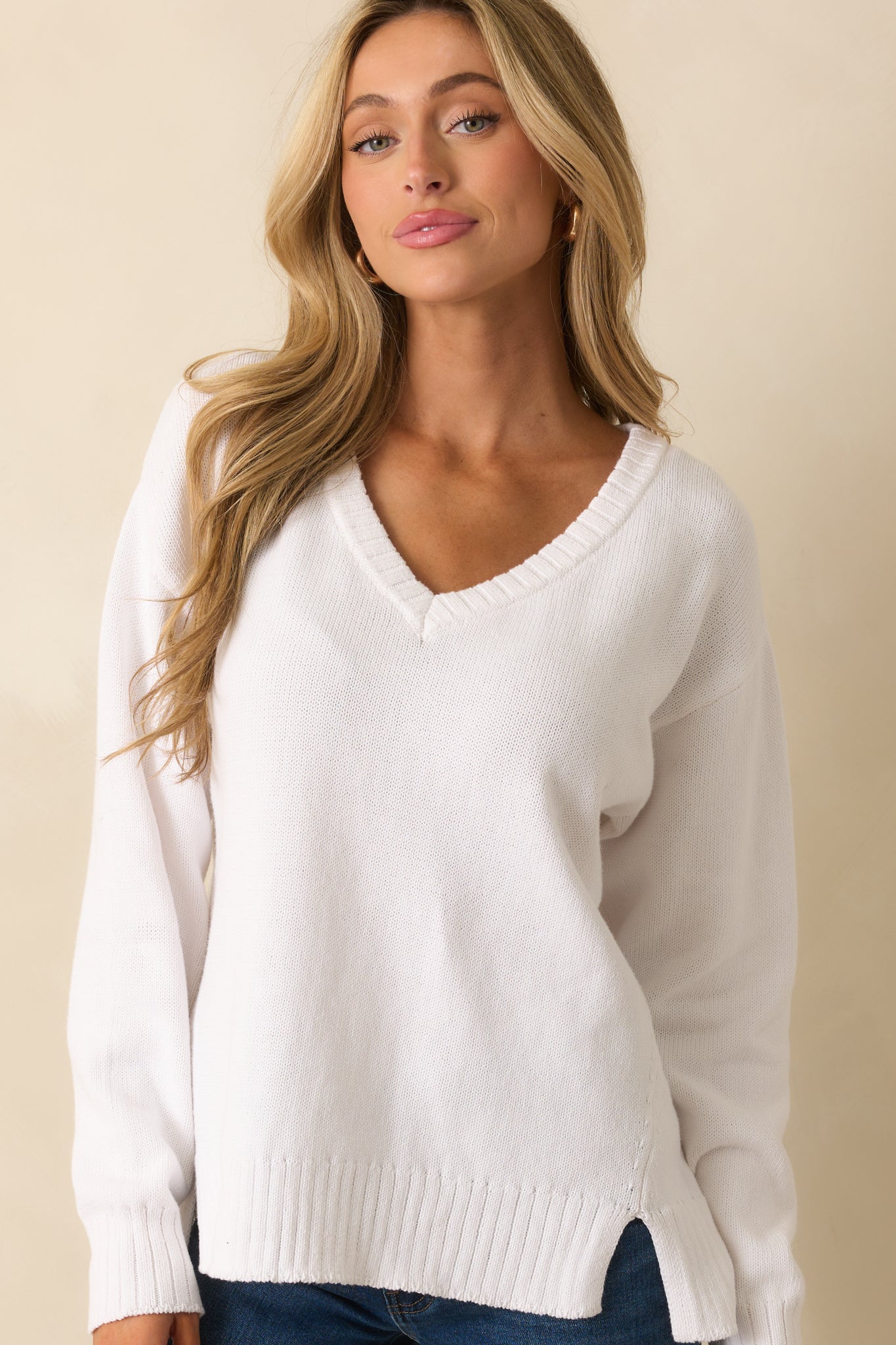 Close crop of v-neckline and drop shoulder detailing on white cotton sweater.
