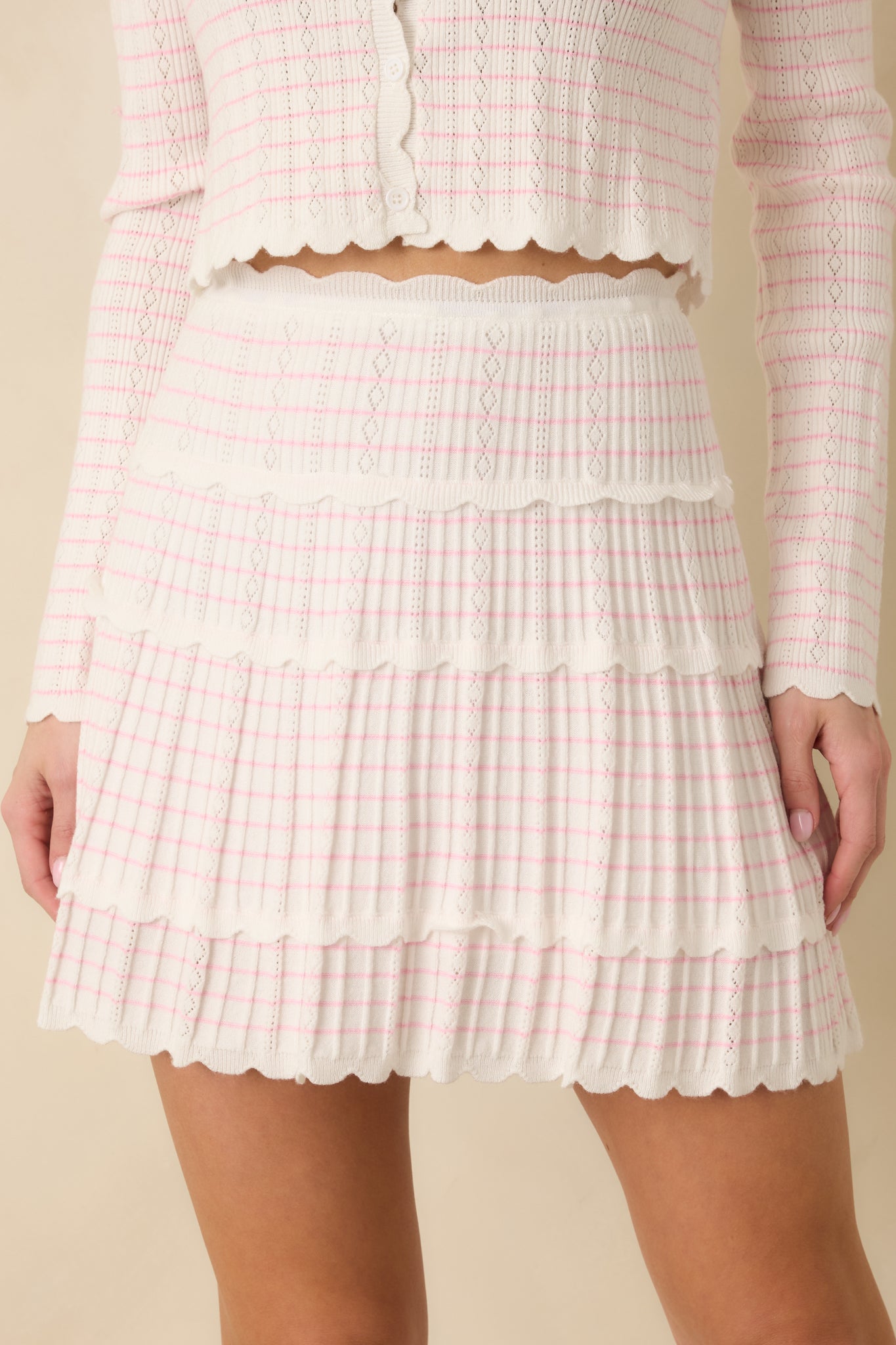 Close-up detail of the white mini skirt showing scalloped trim, pink stripe pattern, and fabric texture.