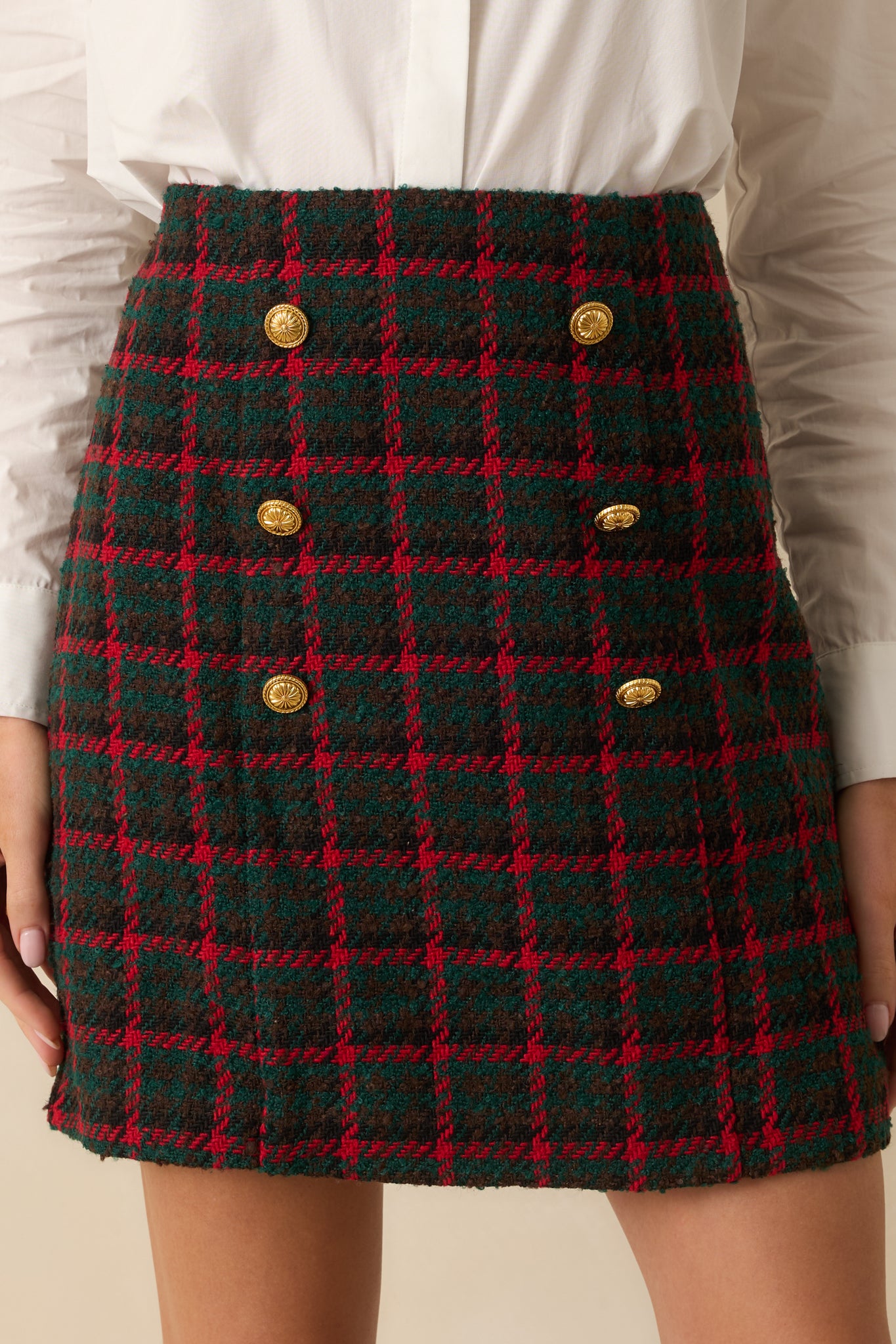 Close focus on the plaid pattern and polished gold buttons that define the skirt’s crisp silhouette.