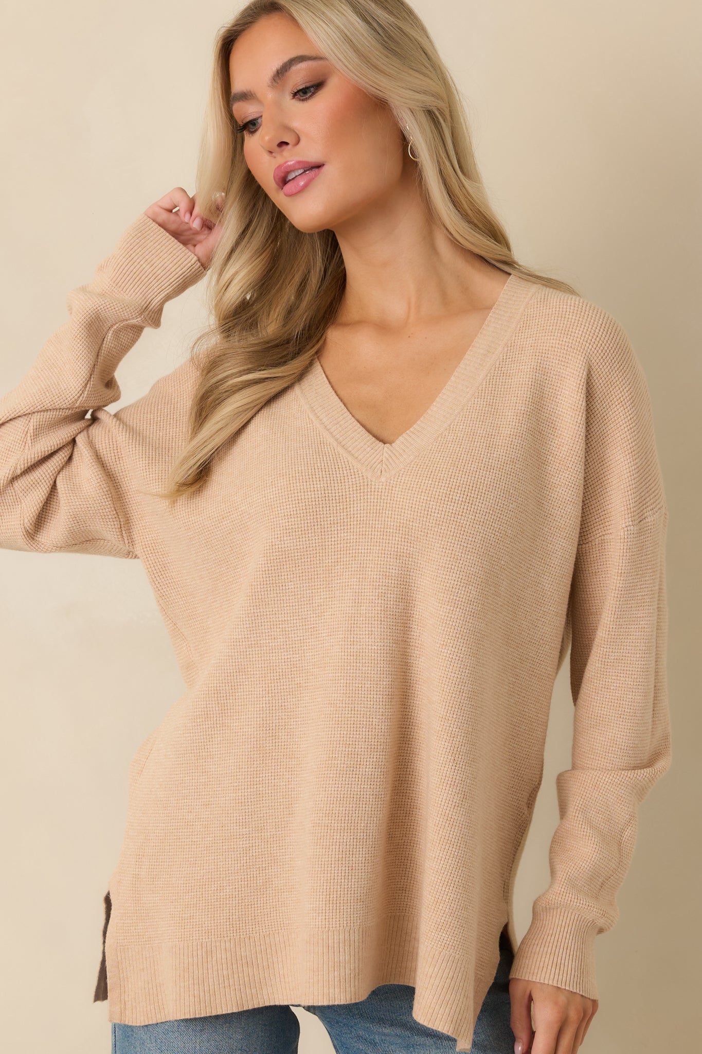 Close look at light taupe sweater highlighting long sleeves, split hem, and soft knit texture.