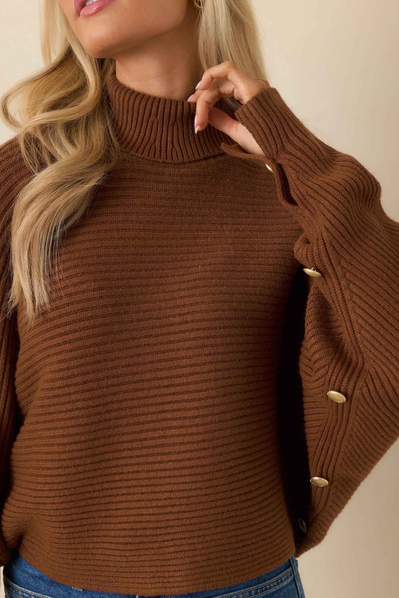 Close-up of brown sweater cuff with small decorative buttons and ribbed texture.