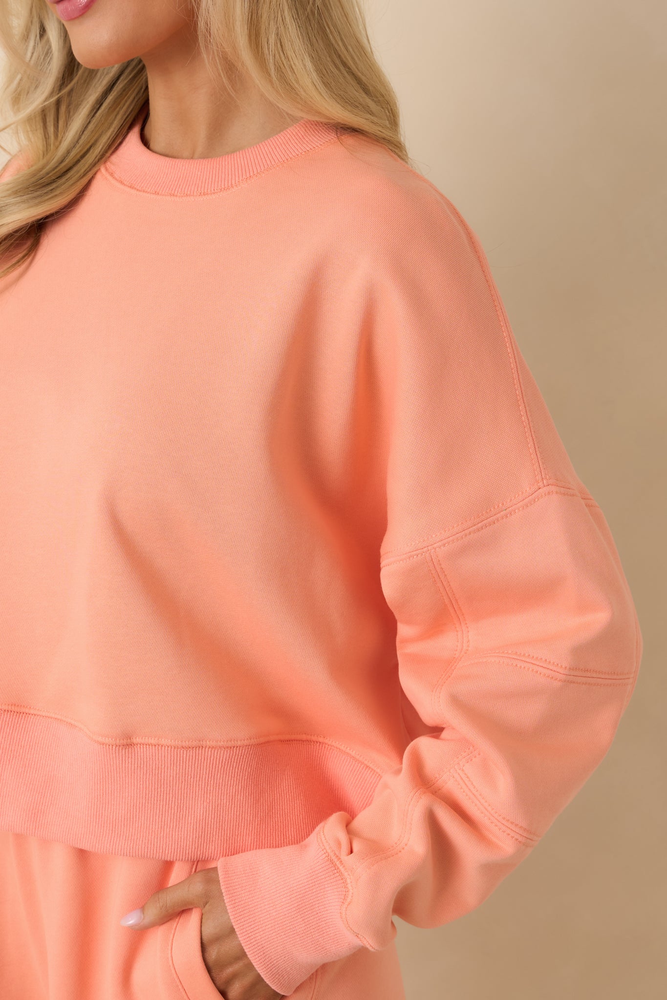 Close-up of ribbed hem and block-stitched sleeve on coral knit sweatshirt.