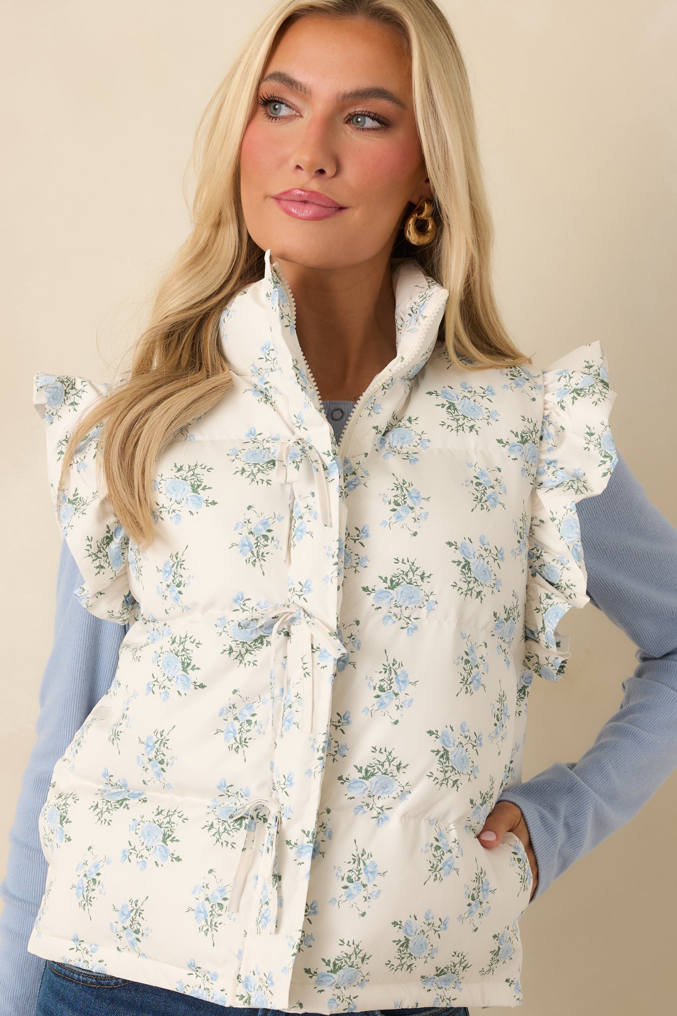 Close view of the ivory puffer vest highlighting the front ties, quilted blue floral stitching, and frilled trim at the arm openings.