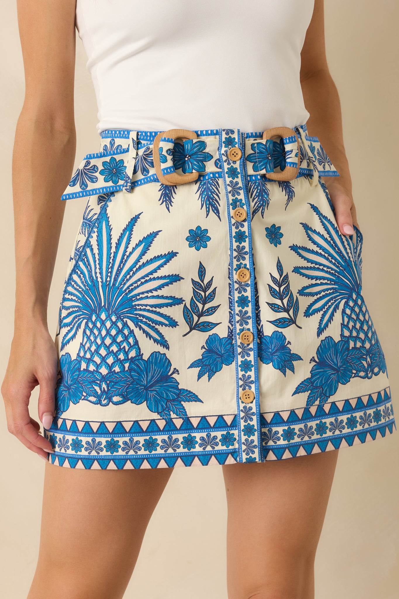Close-up of the tropical mini skirt detailing the button-front placket, belt, and printed fabric.