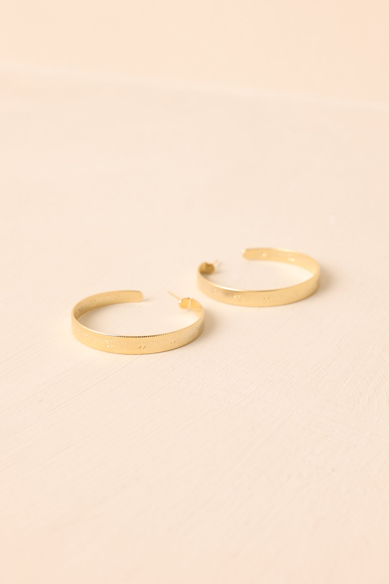 A close-up shot of the incomplete hoop earrings with a textured ruler pattern shown against a beige backdrop.