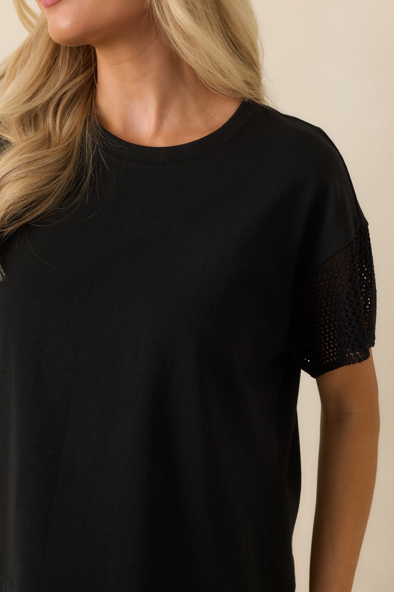 Close-up of the black top highlighting the soft cotton and lyocell blend, crew neckline, and intricate crochet sleeve detailing.