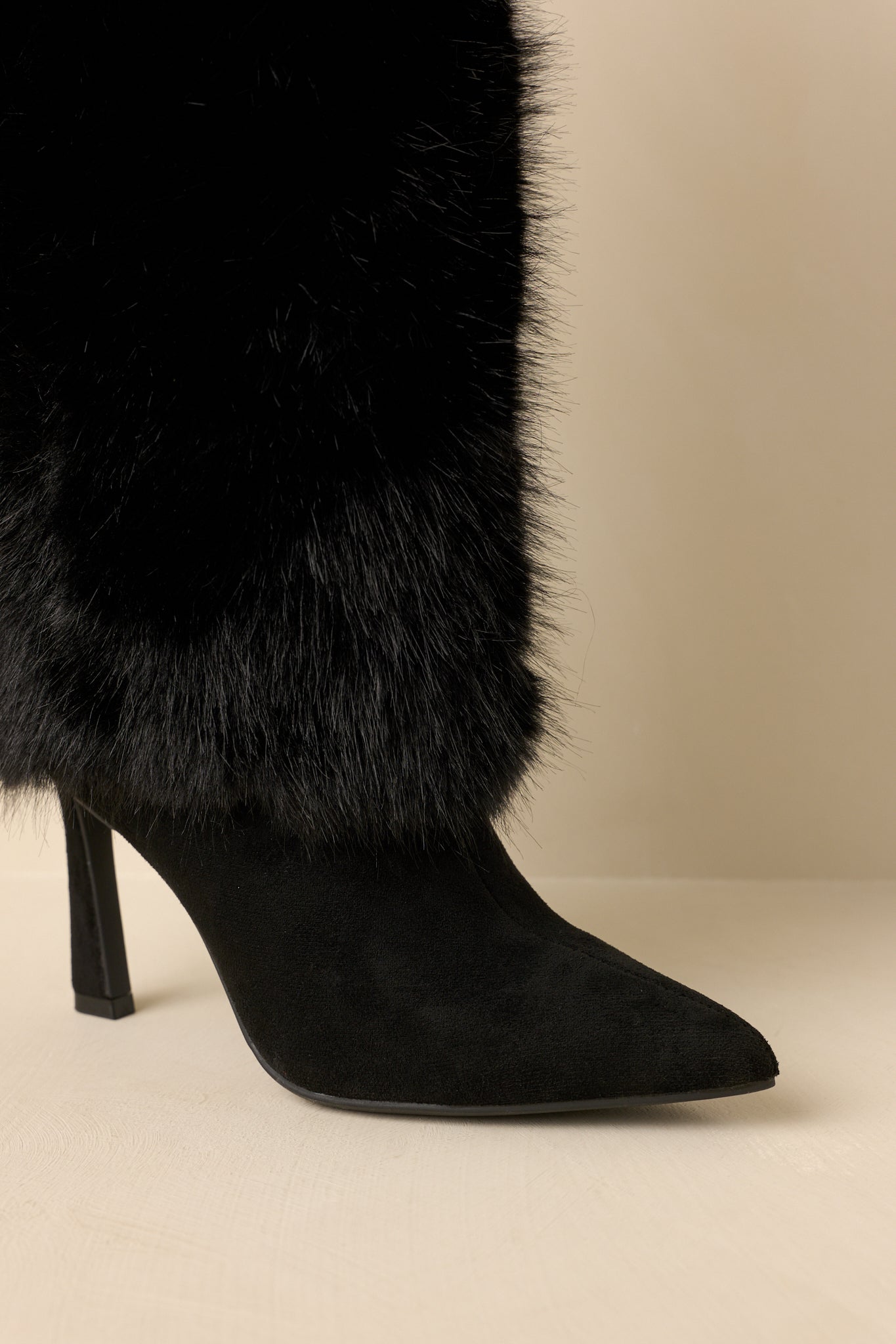 Close-up detail of the black stiletto boots showing the plush faux fur shaft, pointed toe, and suede texture.