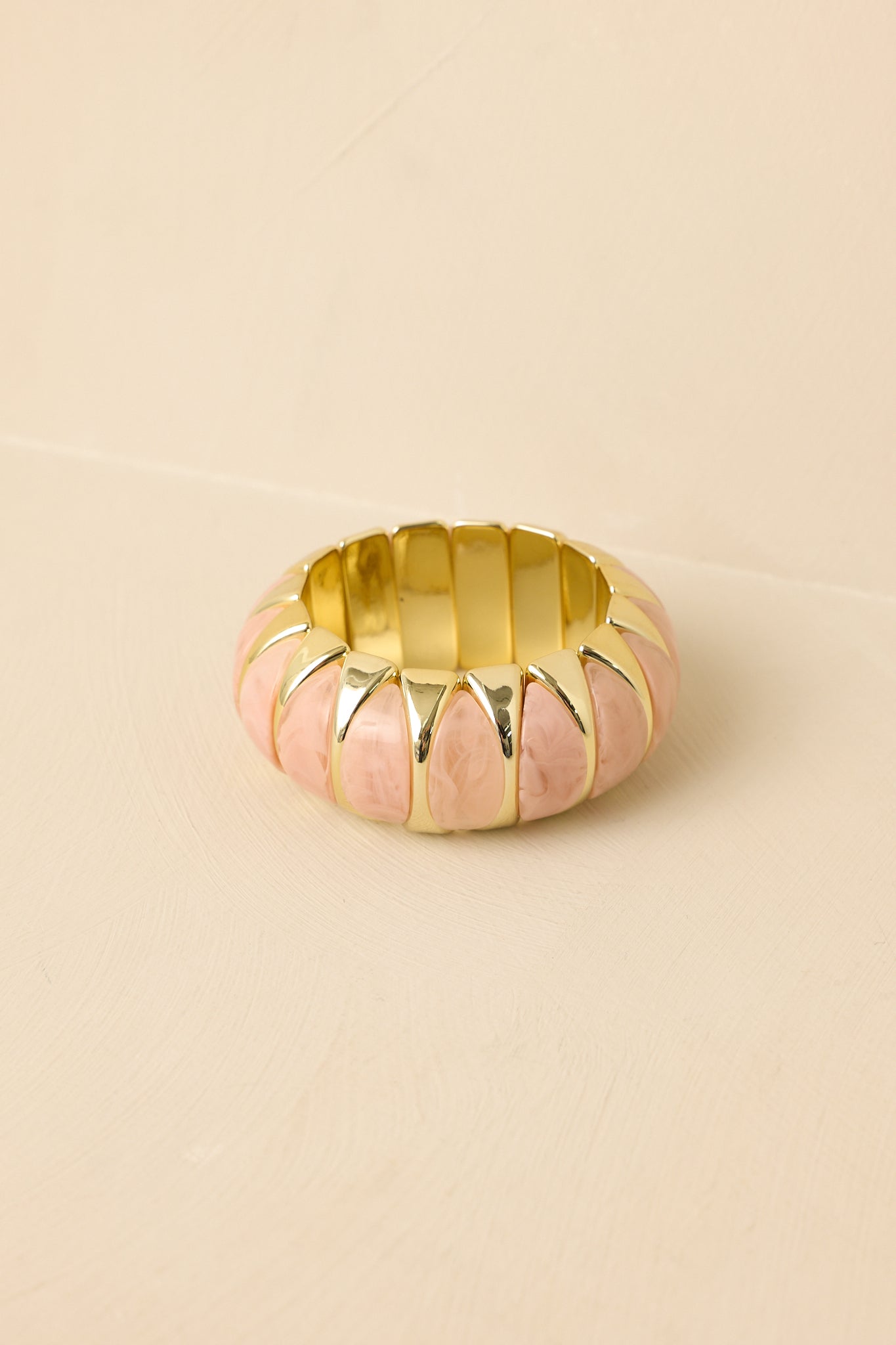 Close-up of bracelet detailing polished gold-tone settings holding pink beads, highlighting shine and dimension.