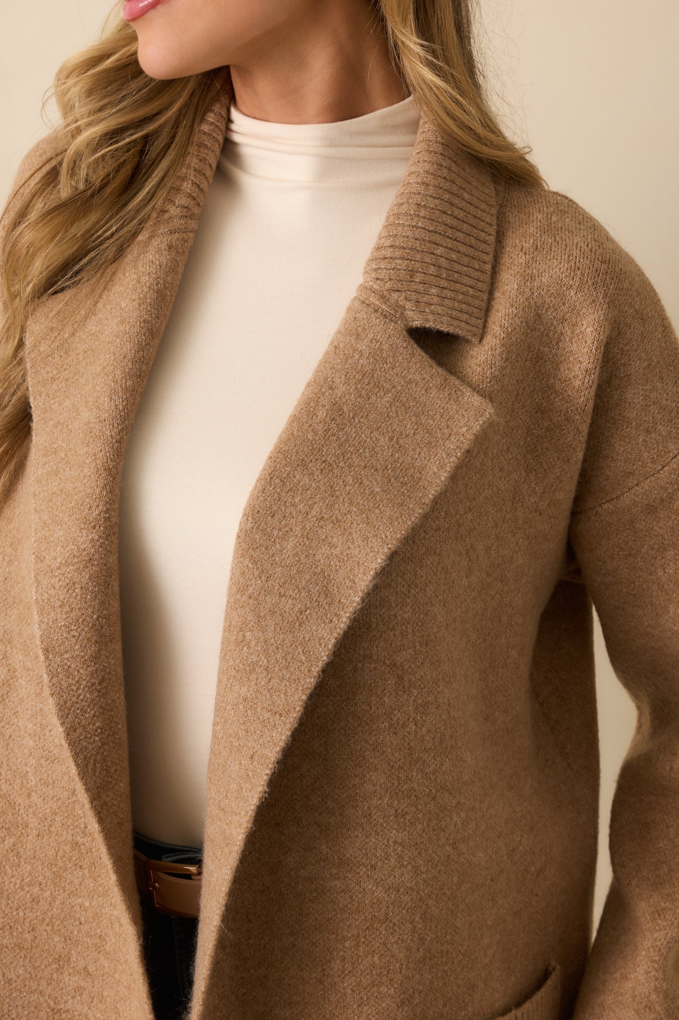 Close-up of camel knit fabric showing ribbed cuffs, patch pocket, and notched lapel collar.