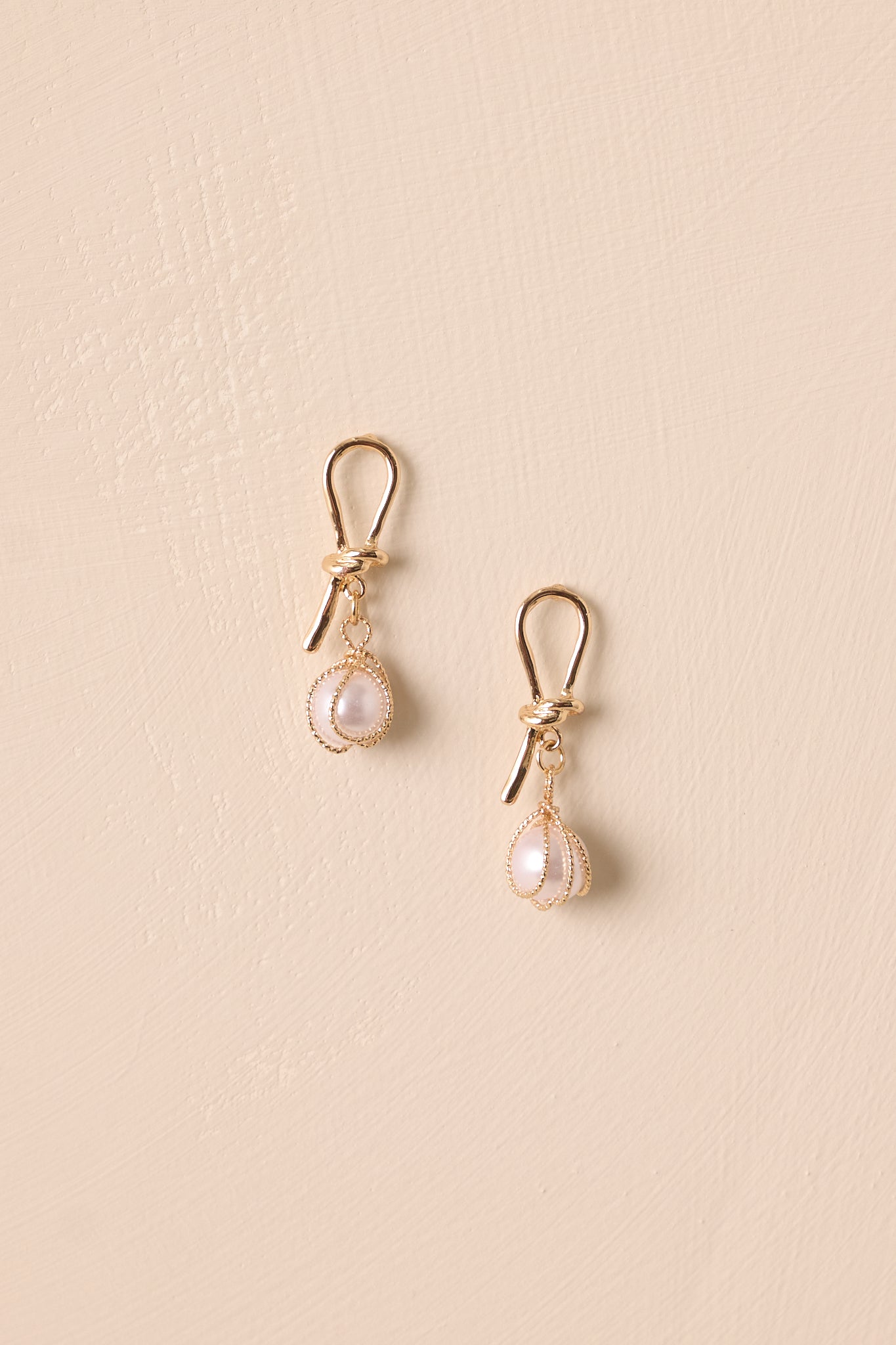 Detailed close-up capturing the textured gold strand, ivory faux pearl, and secure post backing of the earrings.