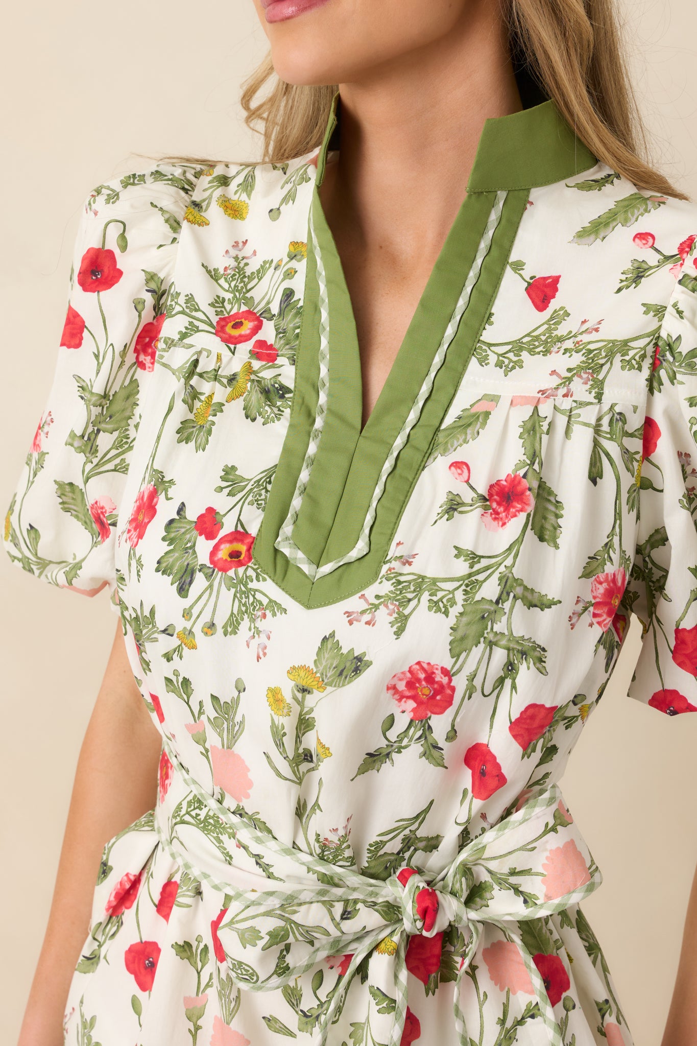 Close-up detail of the olive green dress highlighting the contrast neckline trim and floral belt pattern.