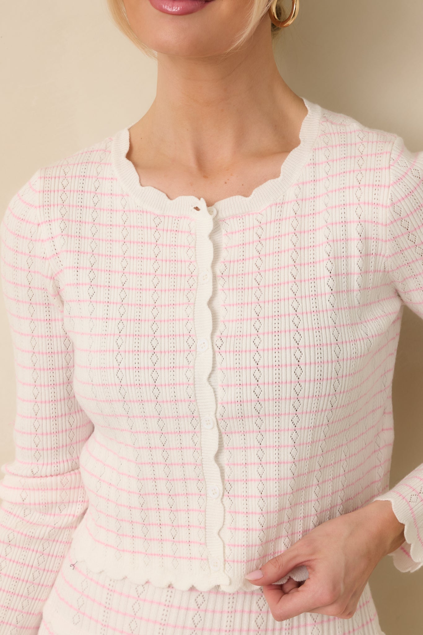 Close-up detail of the white cardigan showing the pink stripe pattern, scalloped trim, and button detail.