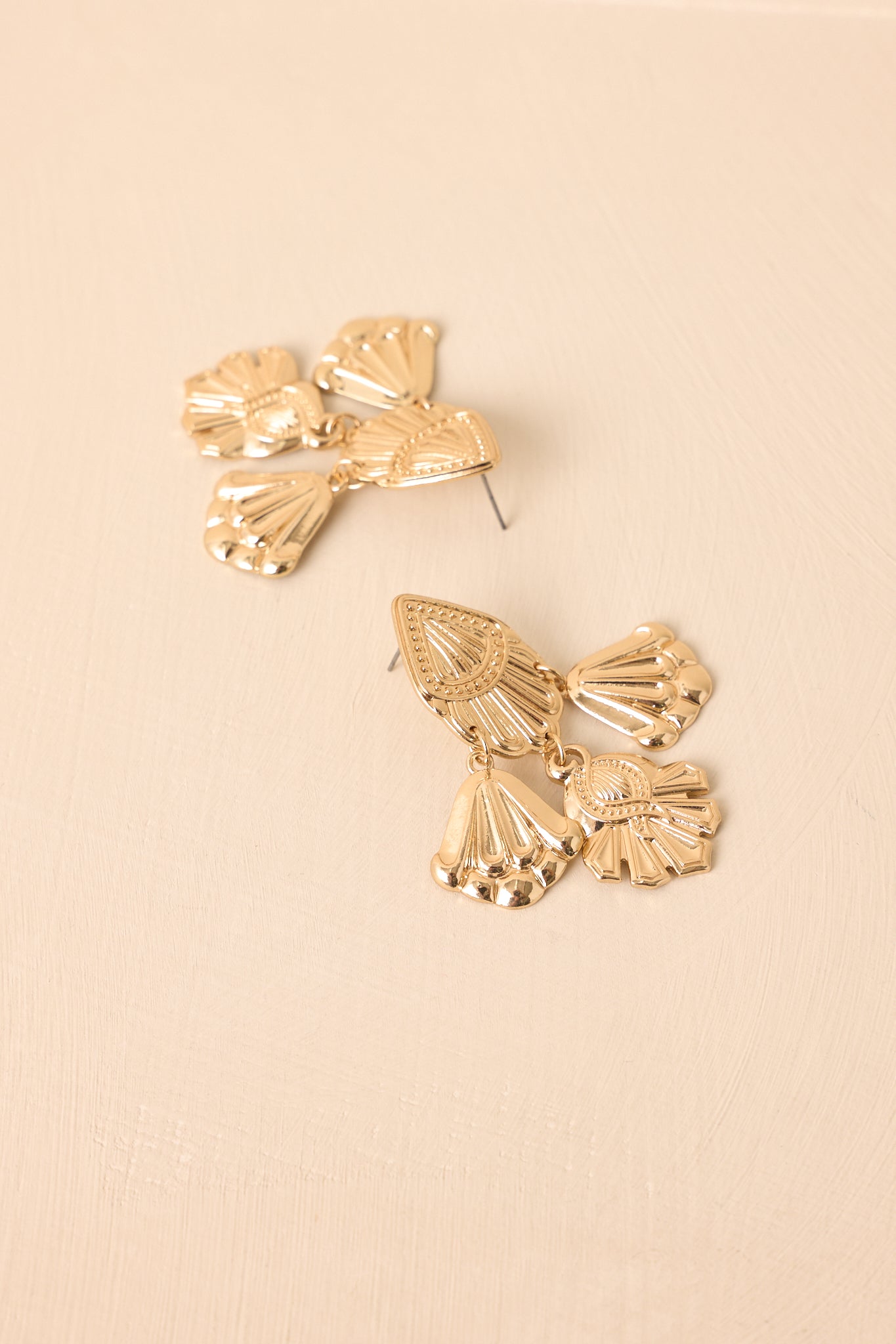 A close-up detailed image revealing the textured gold finish, secure post backing, and dangling charm design.