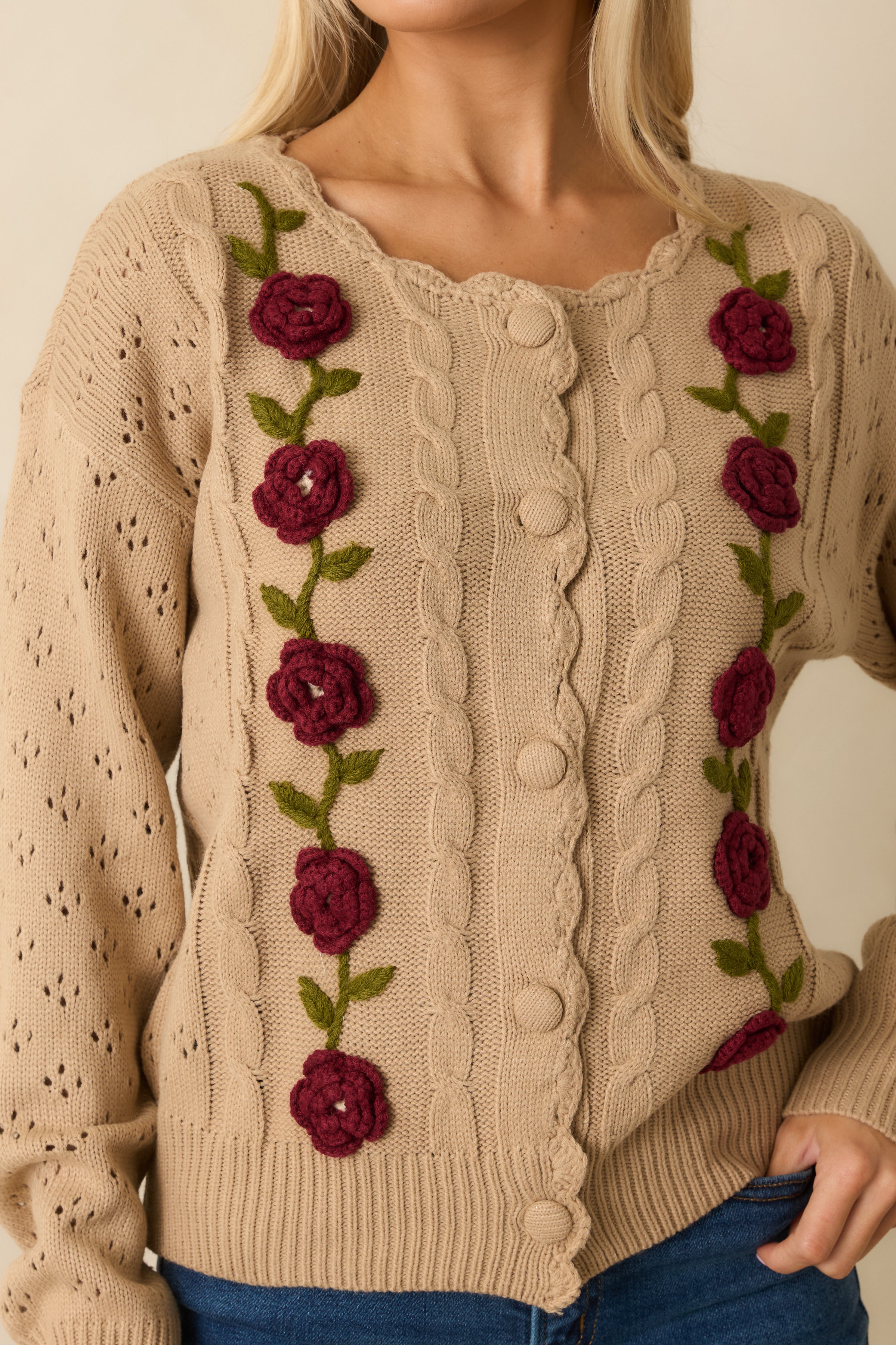 Close-up capturing the dimensional floral appliqué, cable-knit pattern, and tonal buttons.