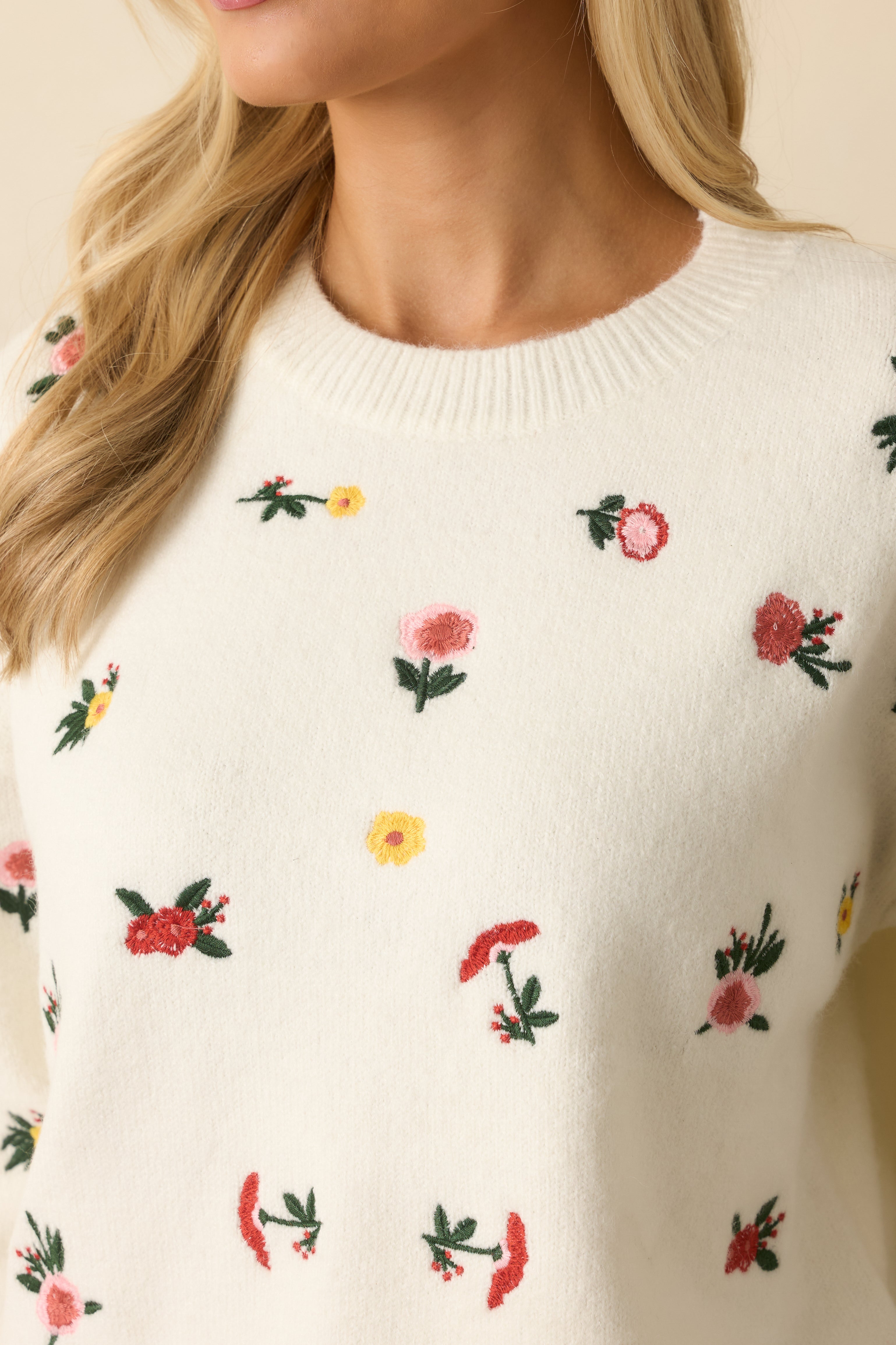 Close-up of the floral embroidery and ribbed crew neckline on the white knit sweater.