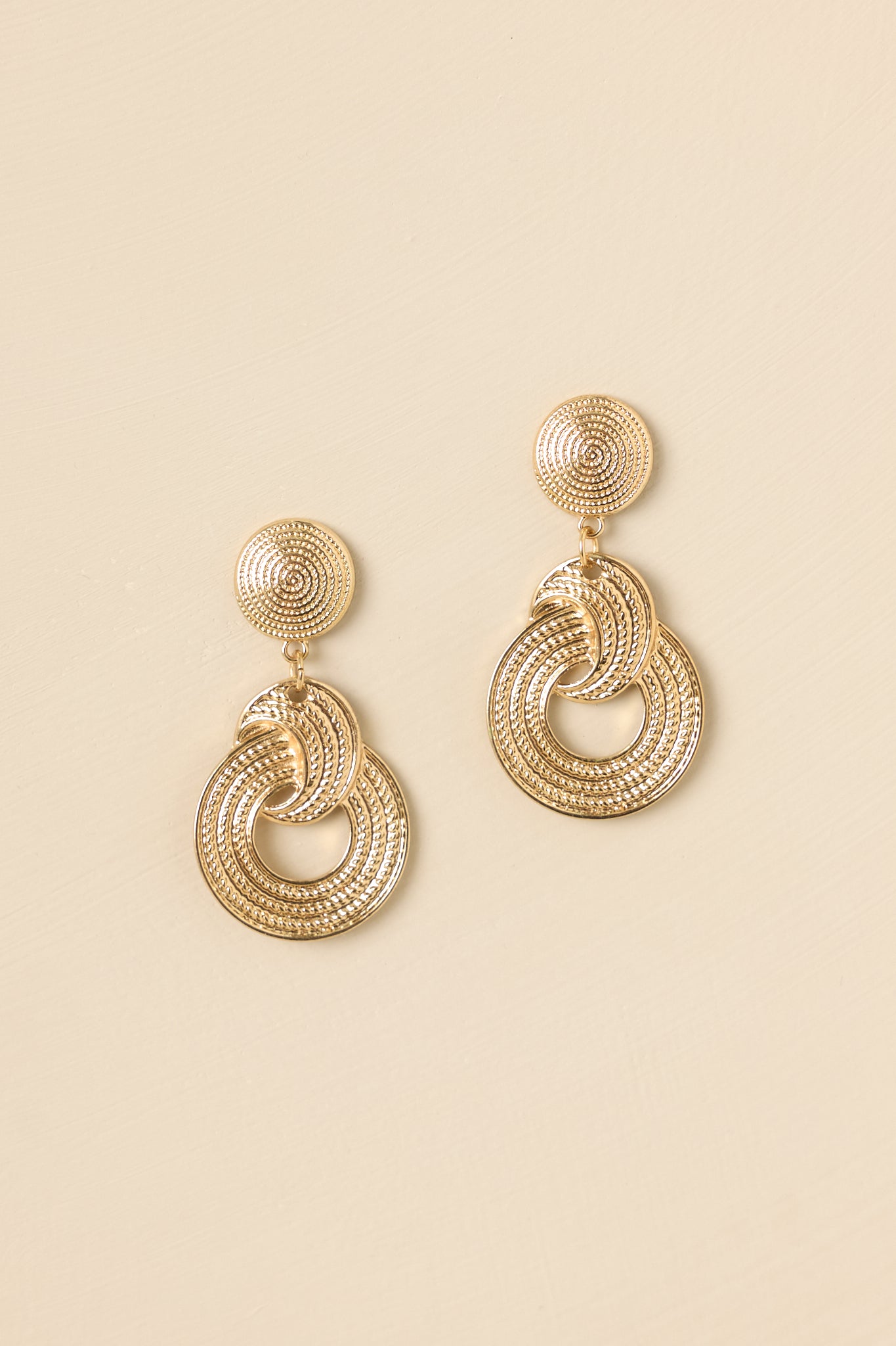 Detailed close-up of the gold drop earrings focusing on the interlocked circular design, textured thread-like finish, and secure post backings.