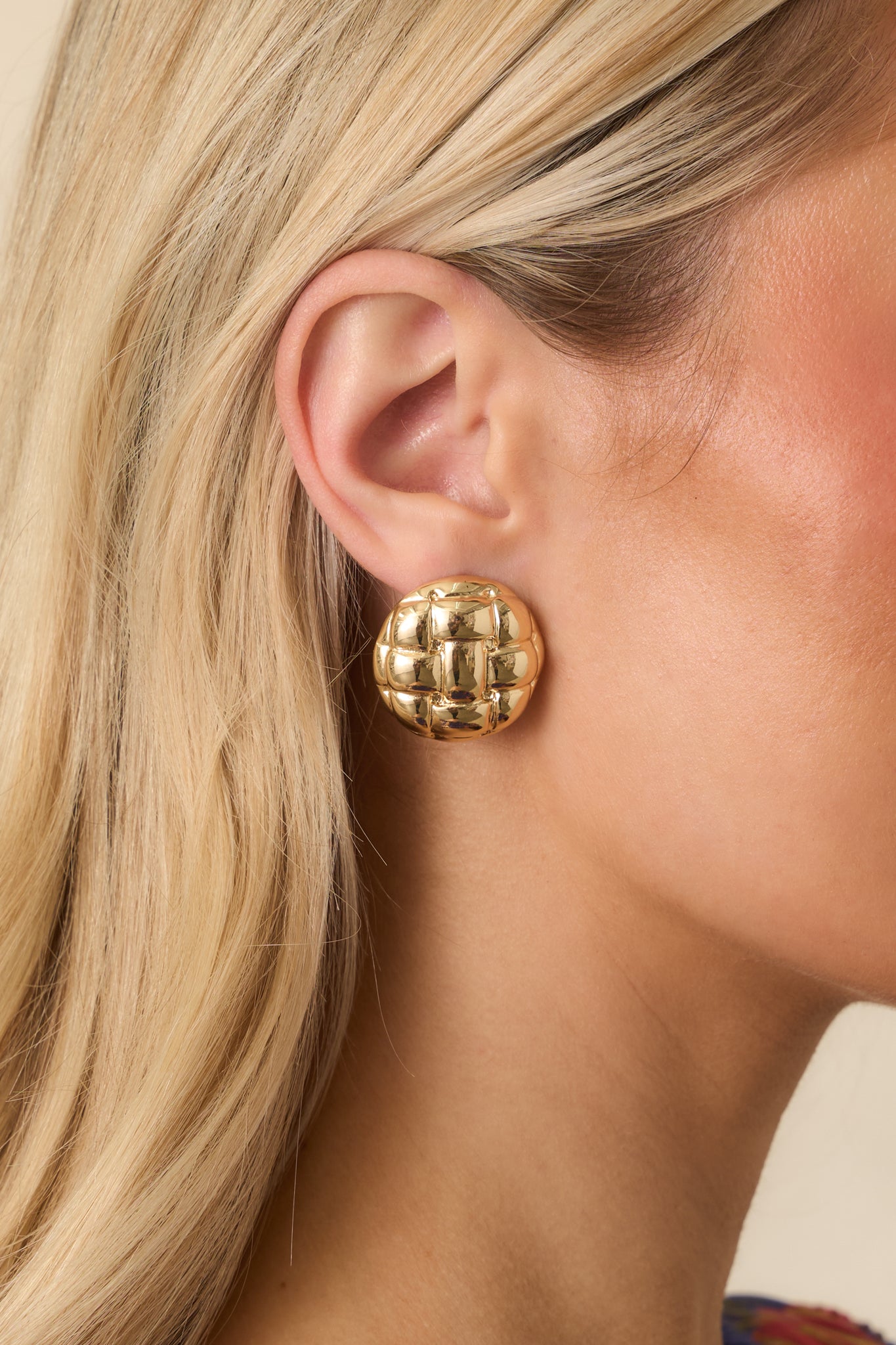 Close-up of circular gold earrings highlighting shiny finish and intricate lattice pattern.