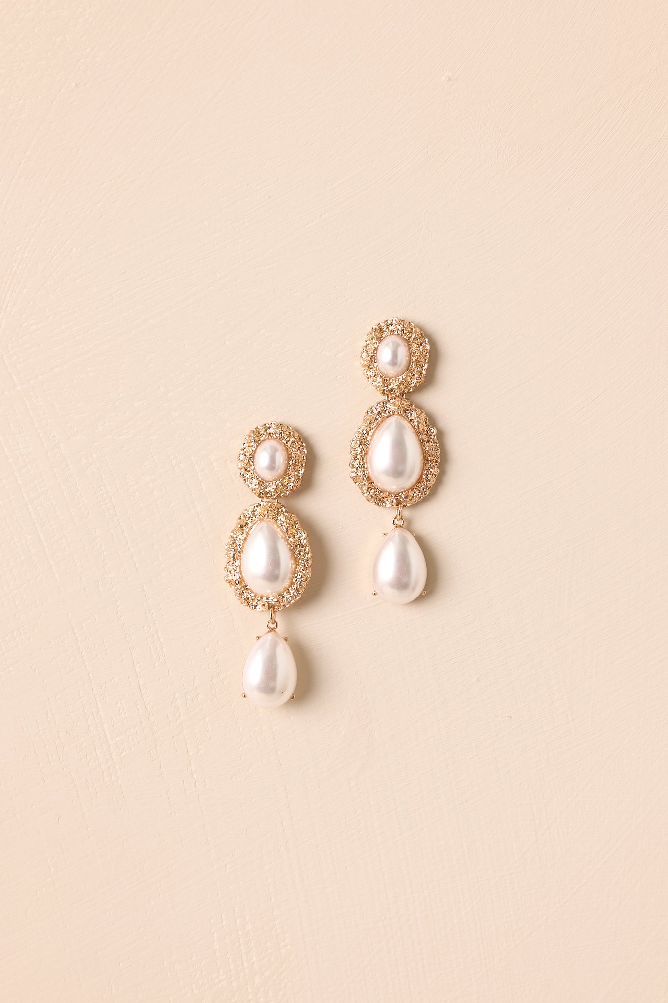 A close-up view of the gold tiered earrings featuring three oval pearl settings and a dangling teardrop pearl.