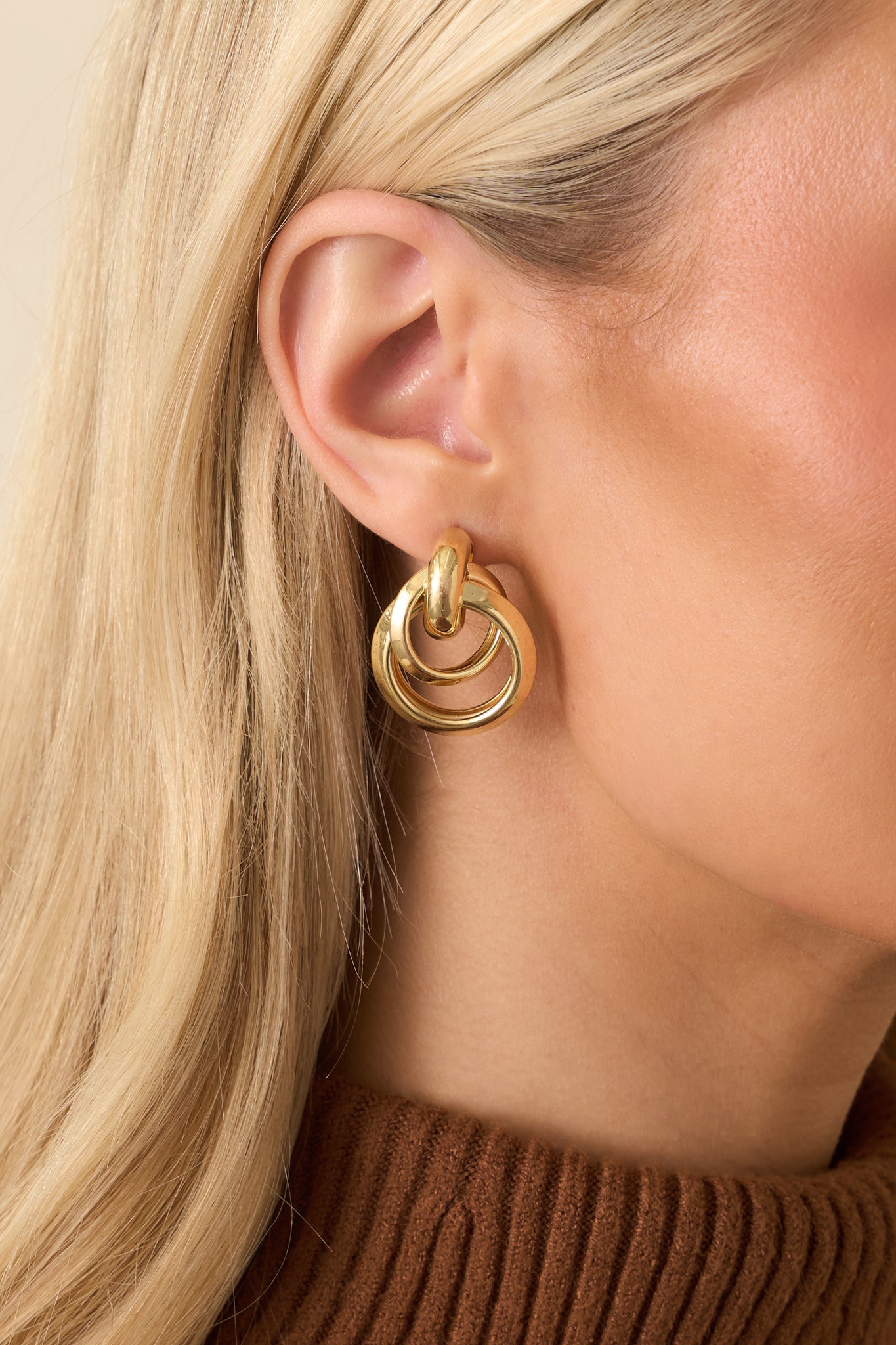 Detailed close-up of the gold-tone drop earrings focusing on the interlocking circle design and smooth polished finish.