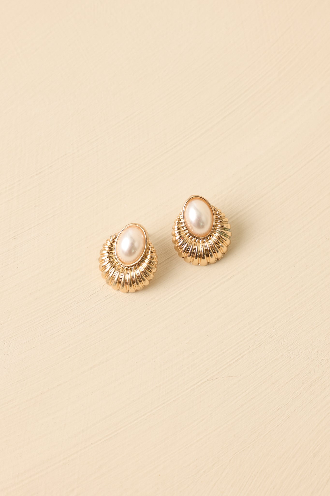 Detailed close-up of the gold-tone stud earrings focusing on the radiating textured gold setting and oval faux pearl centerpiece.
