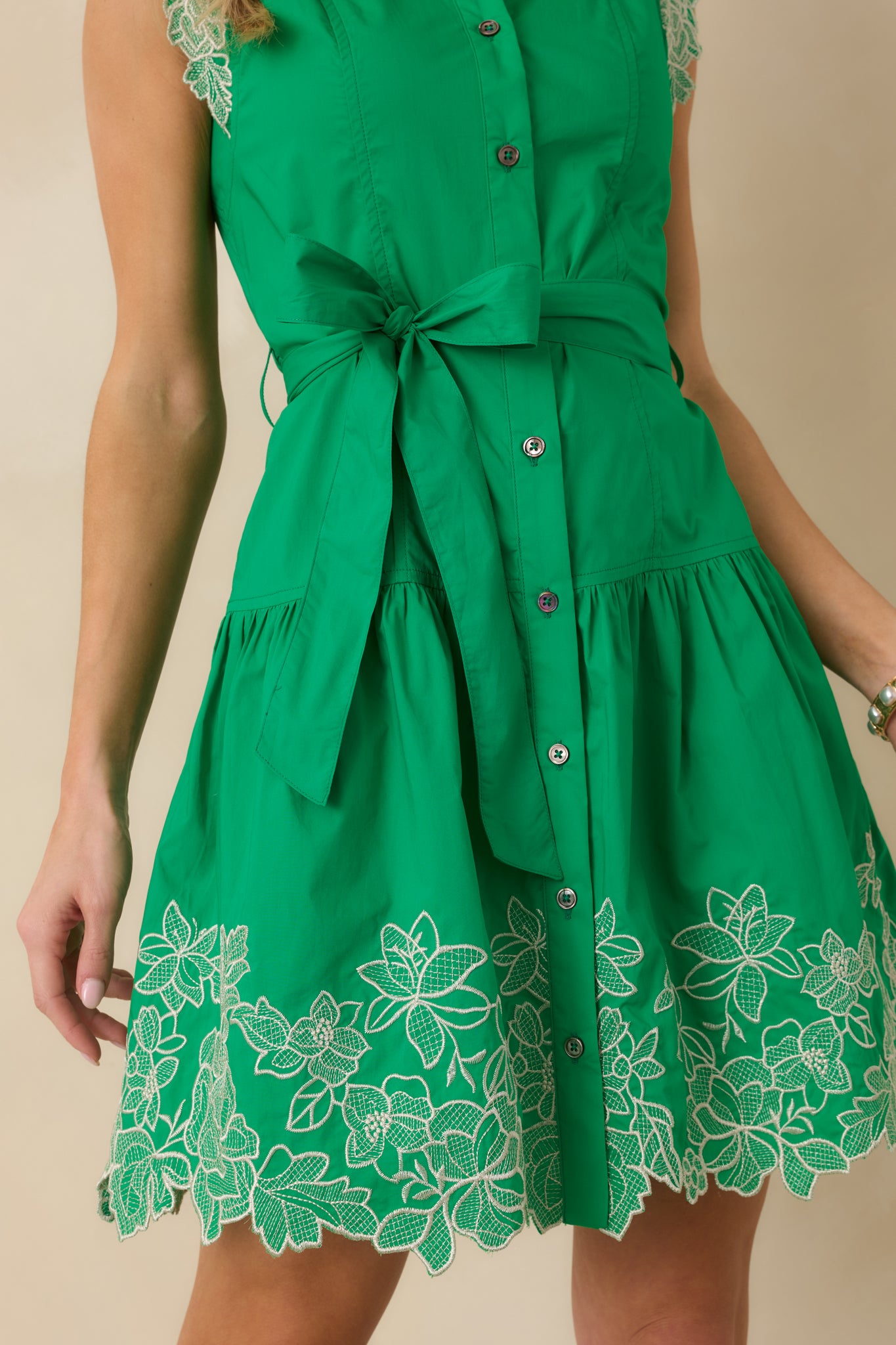 Close-up detail of the green mini dress highlighting the floral embroidery, removable belt, and button-front closure.