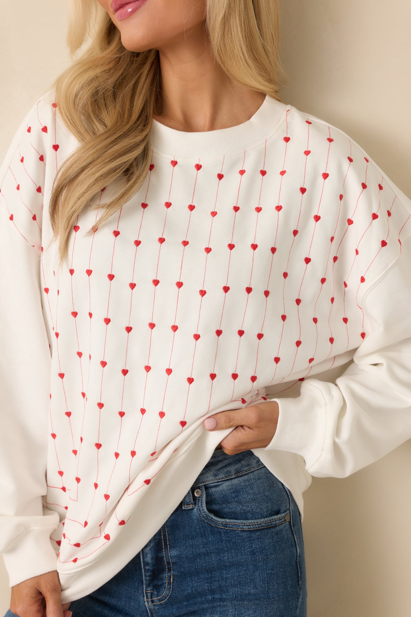 Close-up of soft white knit fabric highlighting raised embroidered hearts stitched in vertical rows across the front of the sweatshirt.