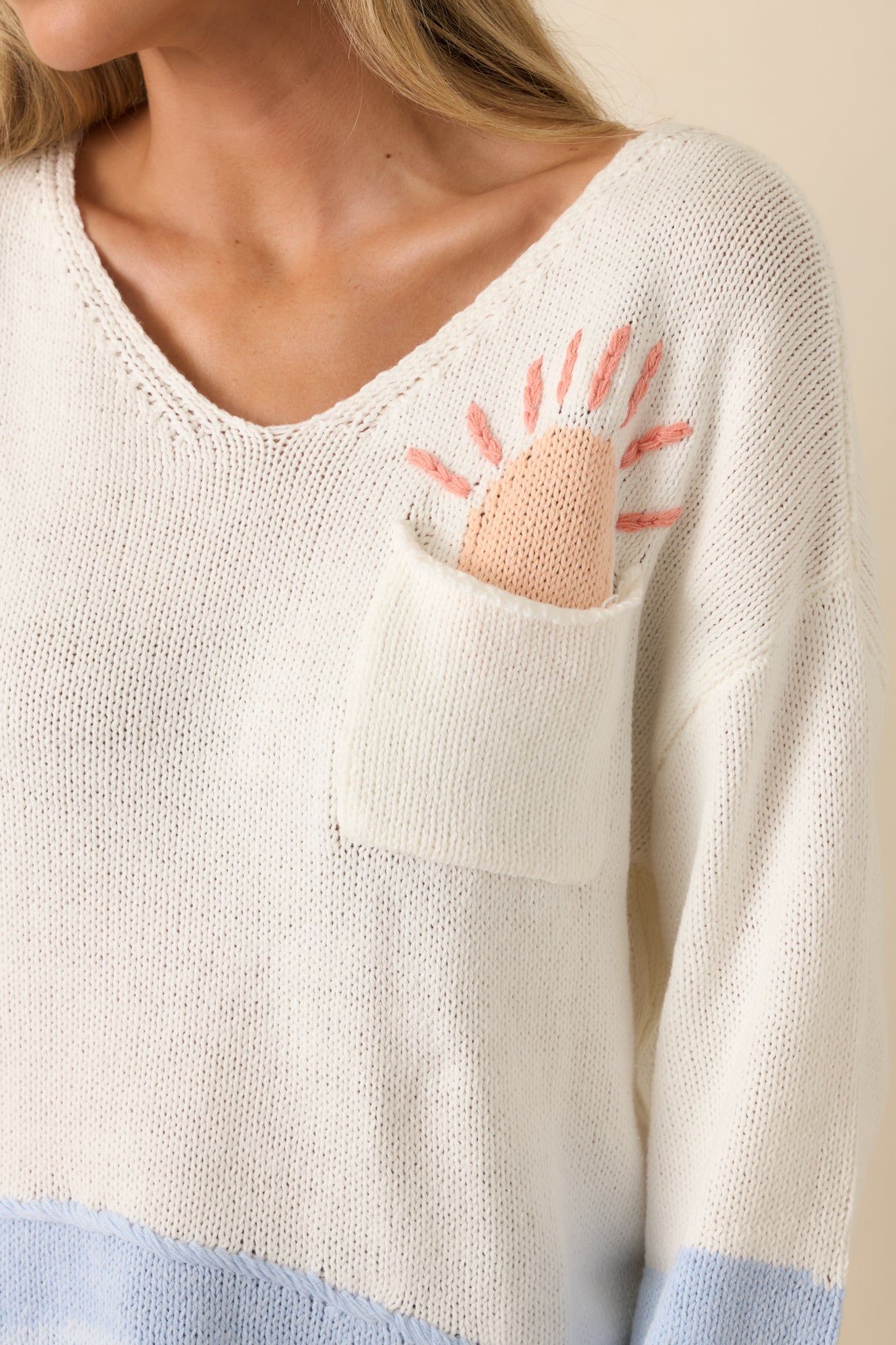 Close-up of the white knit sweater highlighting the pastel blue and blush colorblock accents, knit texture, and sunshine graphic detail.