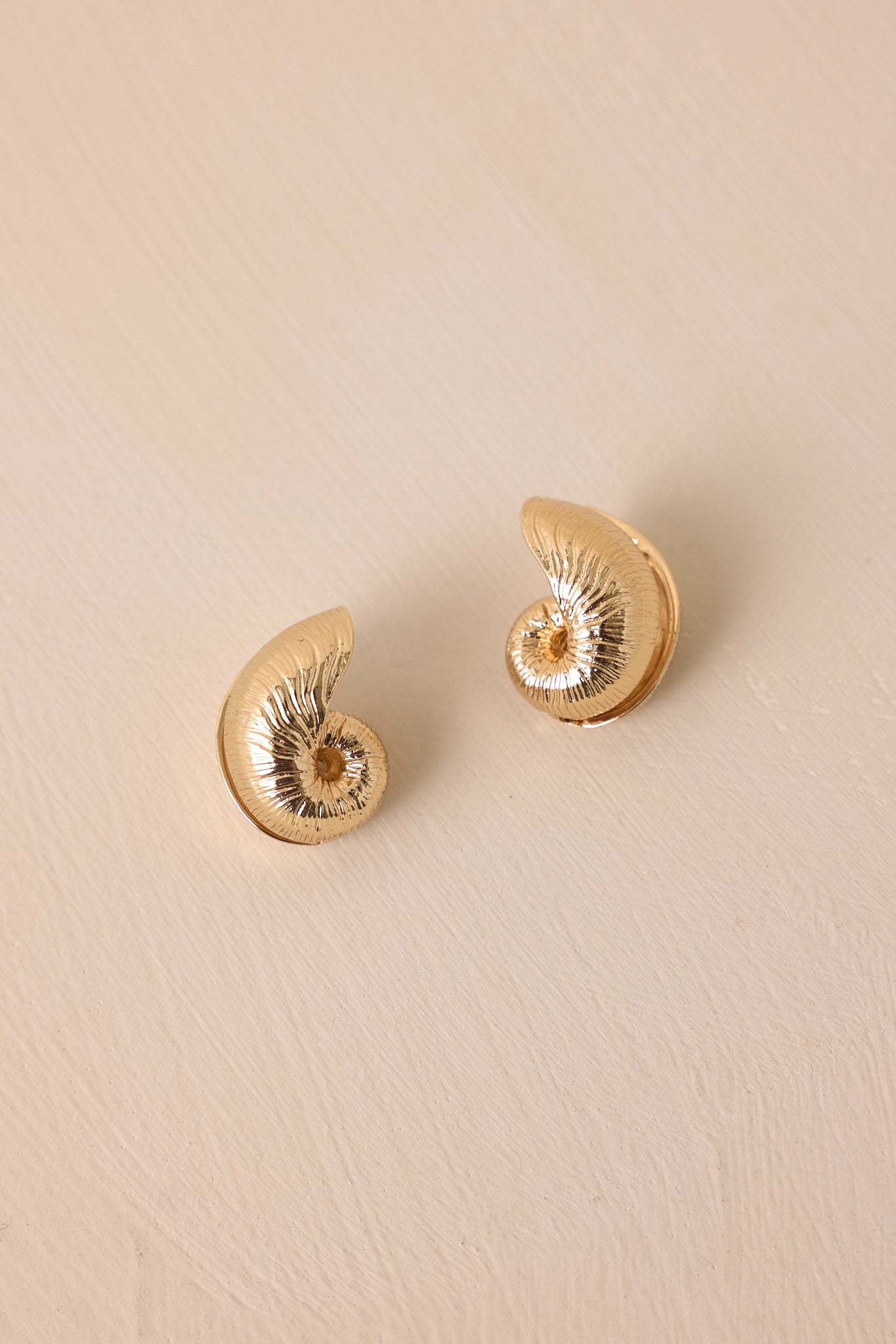 A close-up detail of the huggie earrings showing the intricate gold texture and volute shell shape.