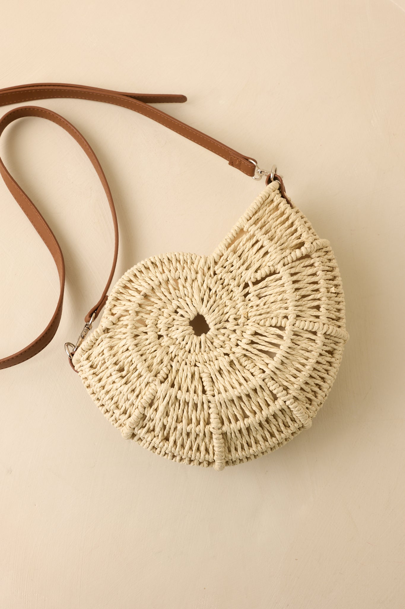 Close-up of ivory crossbody handbag showcasing intricate spiral weaving, metal accents, and lined interior.
