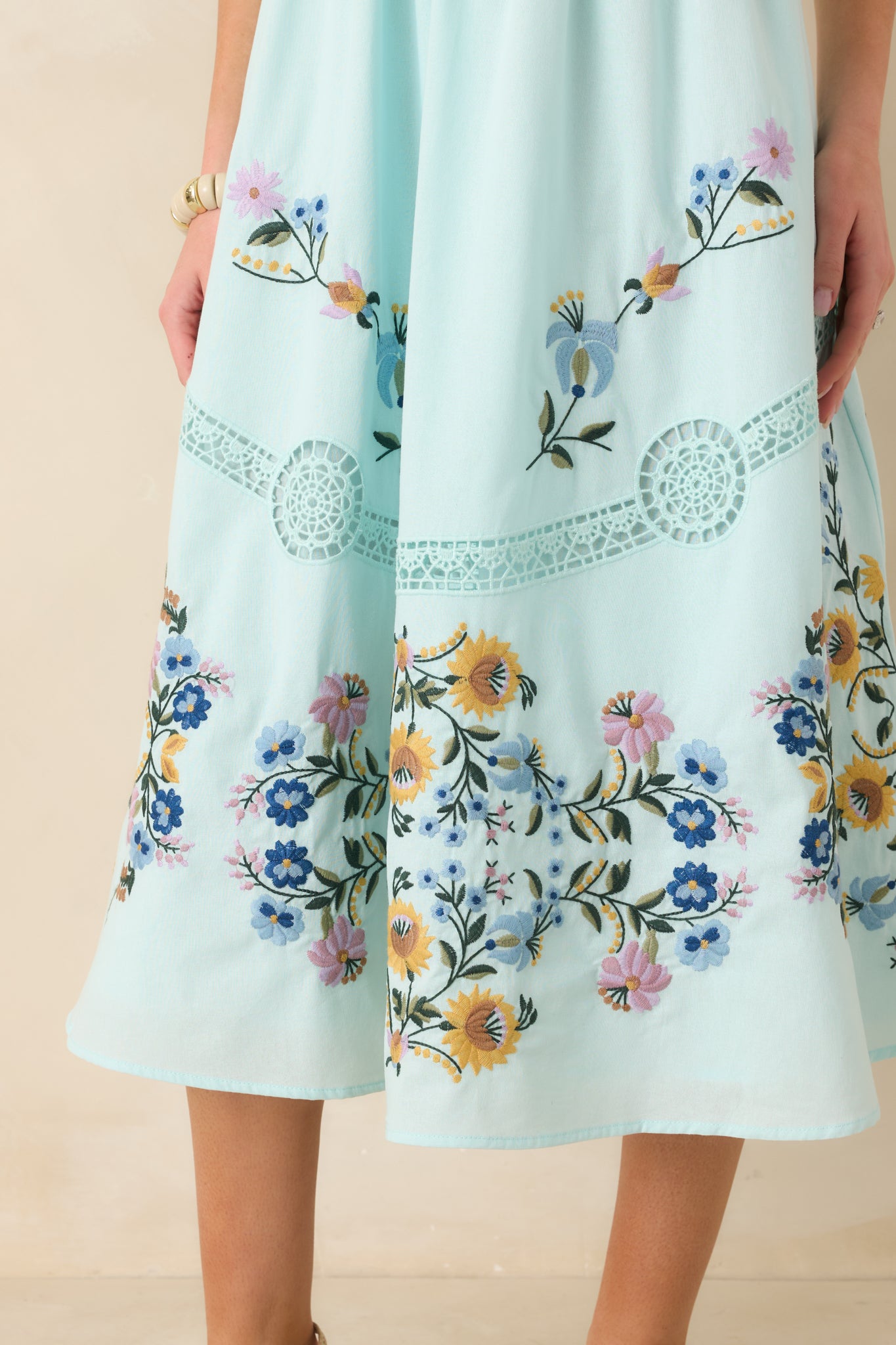 Close-up of light blue fabric showing multicolor floral embroidery and open-ladder lace design.