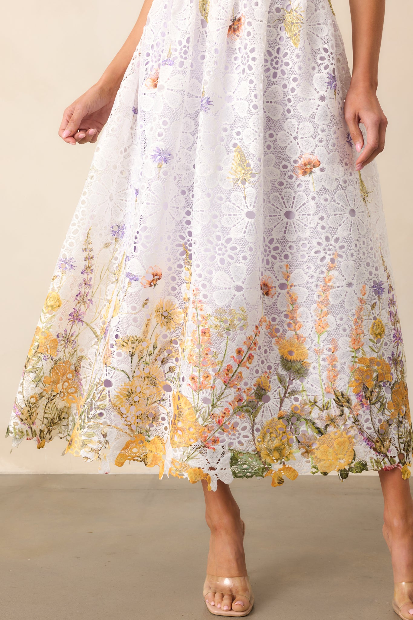 A close-up view of the midi dress’s bottom hemline, showcasing the intricate white and yellow floral embroidery over a soft lavender lining. The eyelet detailing adds texture, while the scalloped edges create a delicate, airy finish.